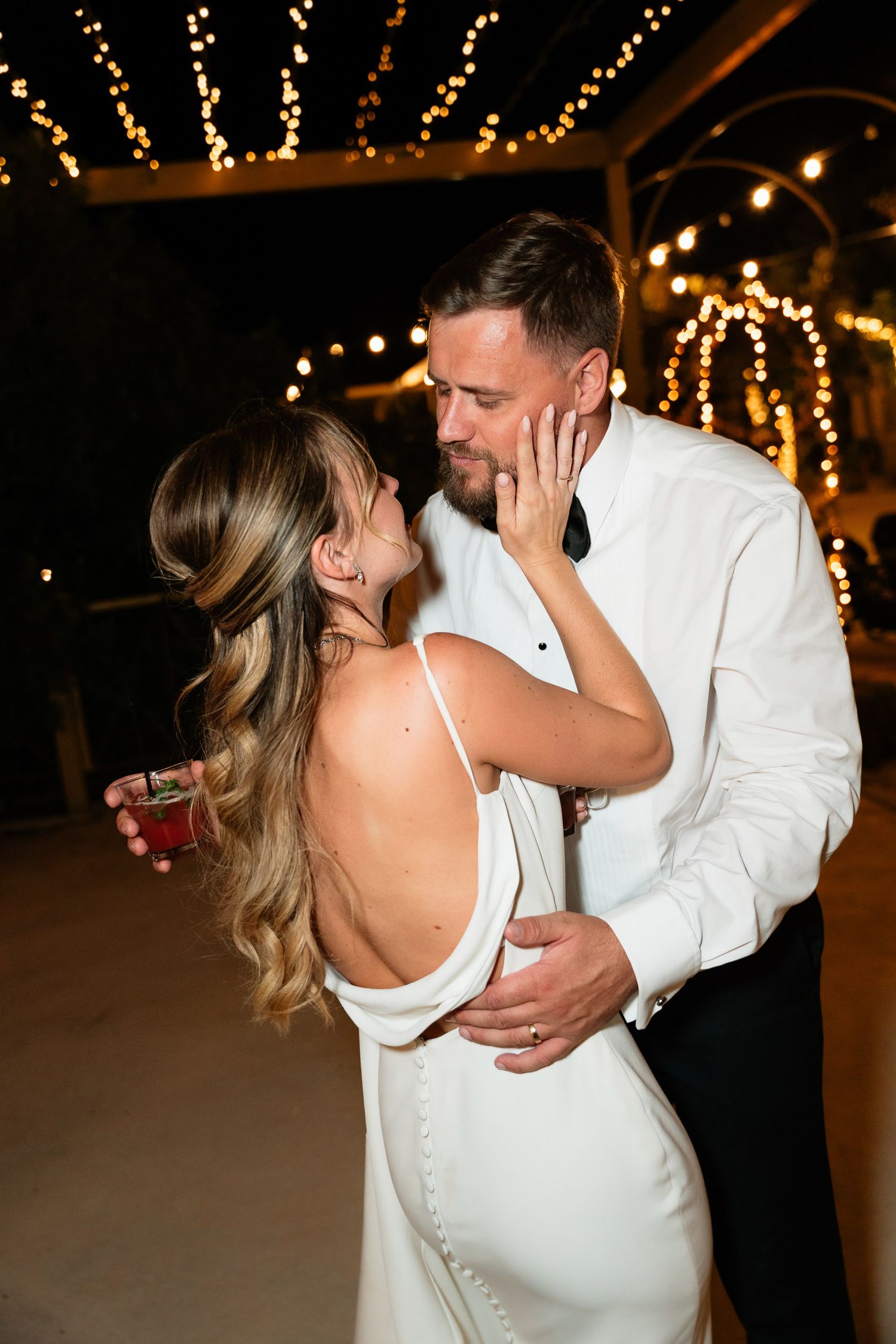 A couple shares a romantic dance moment at their wedding reception with twinkling lights in the background.