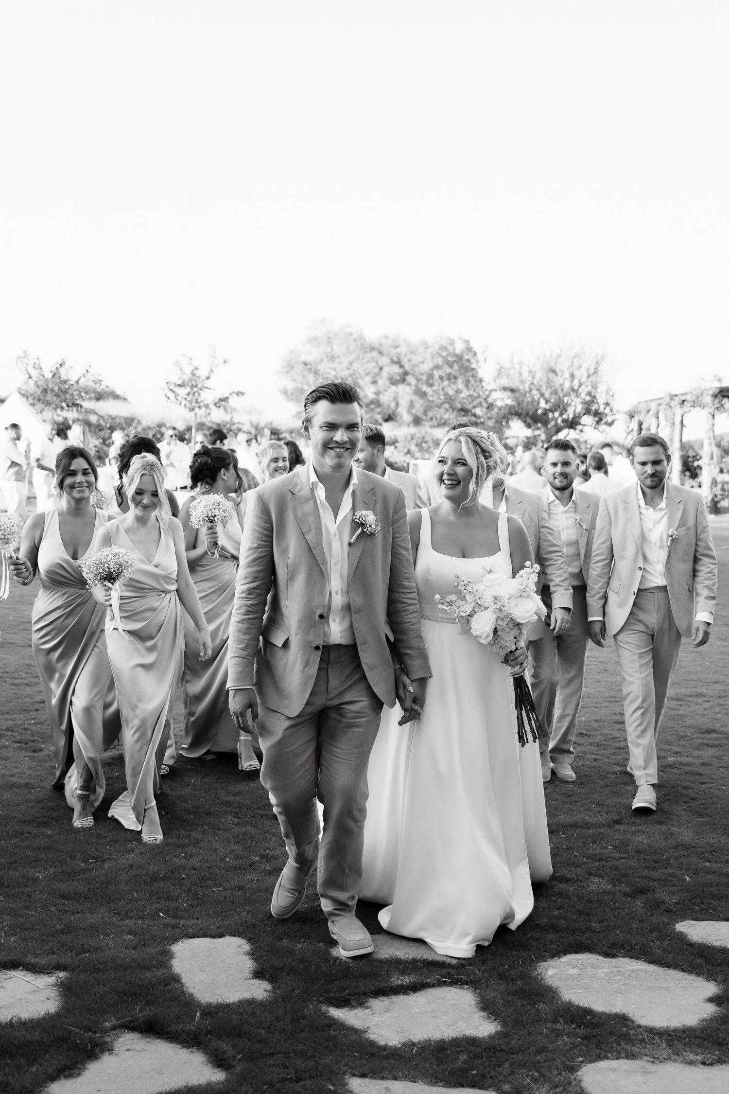 A wedding party walks together across a grassy lawn in a sequence of black and white photographs.