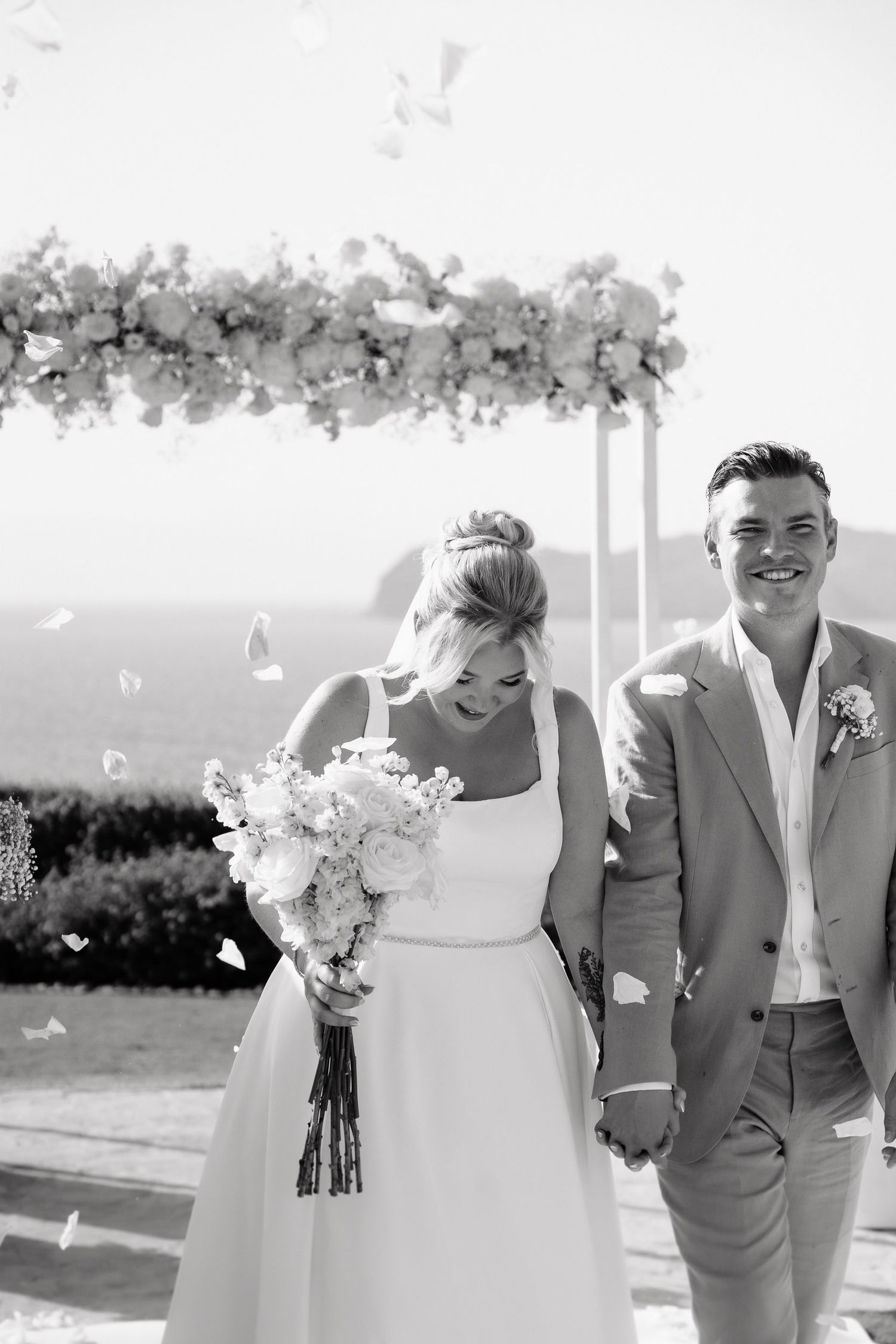 Black and white wedding photos show a couple laughing and walking together outdoors in formal attire with floral bouquets.