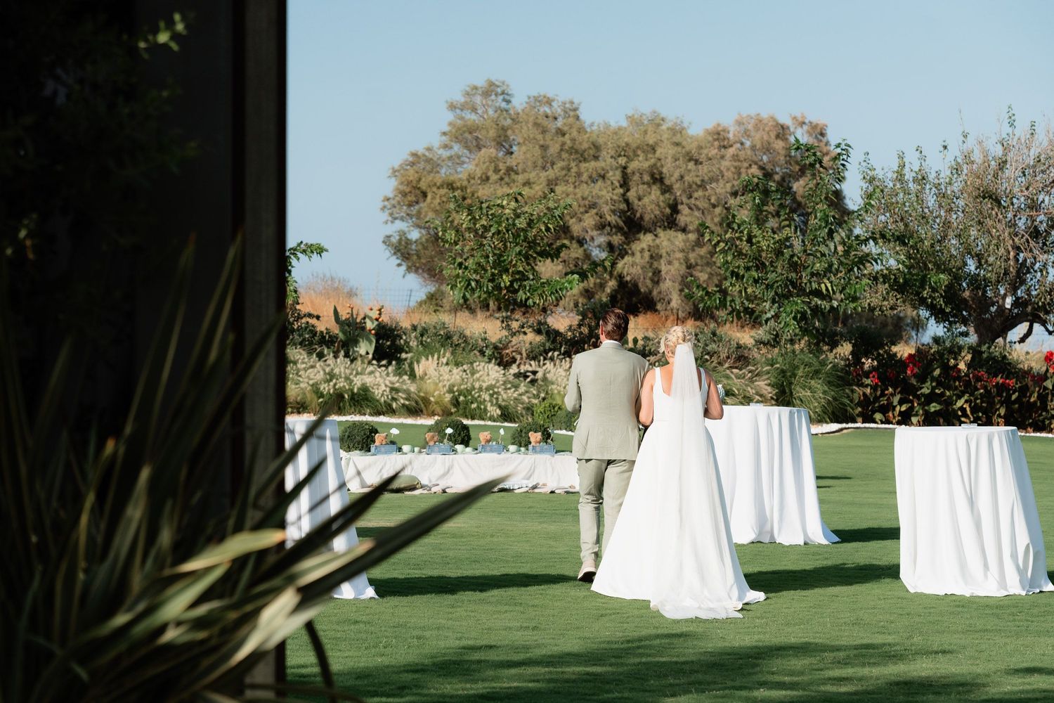 A series of wedding dresses displayed outdoors on mannequins on a green lawn with trees in the background.