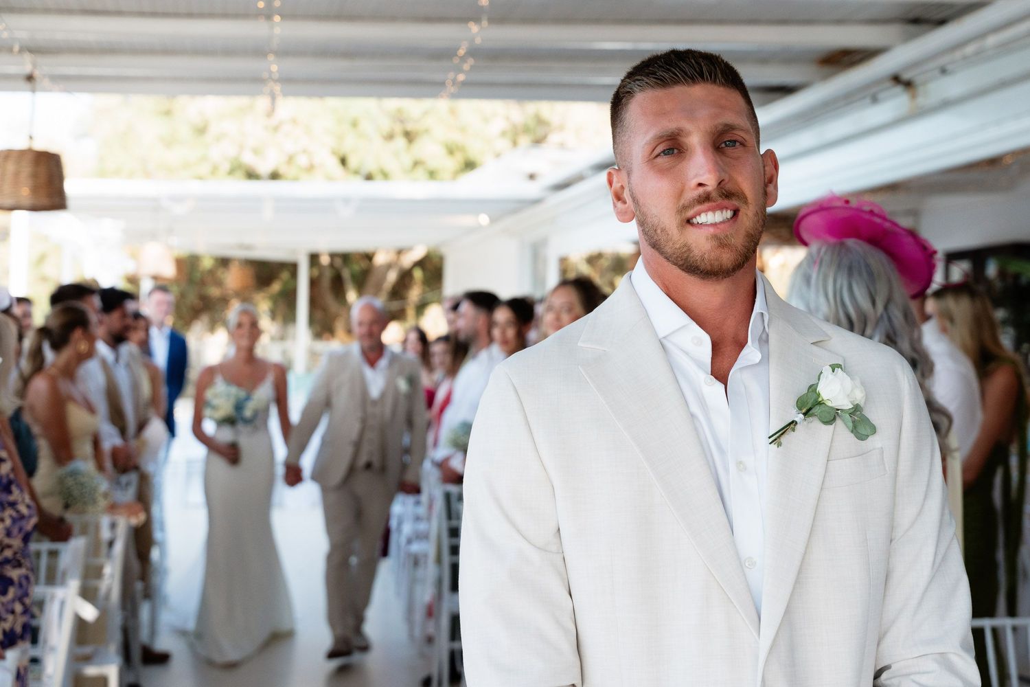 Wedding party members in white attire gather under a covered outdoor venue during a celebration.