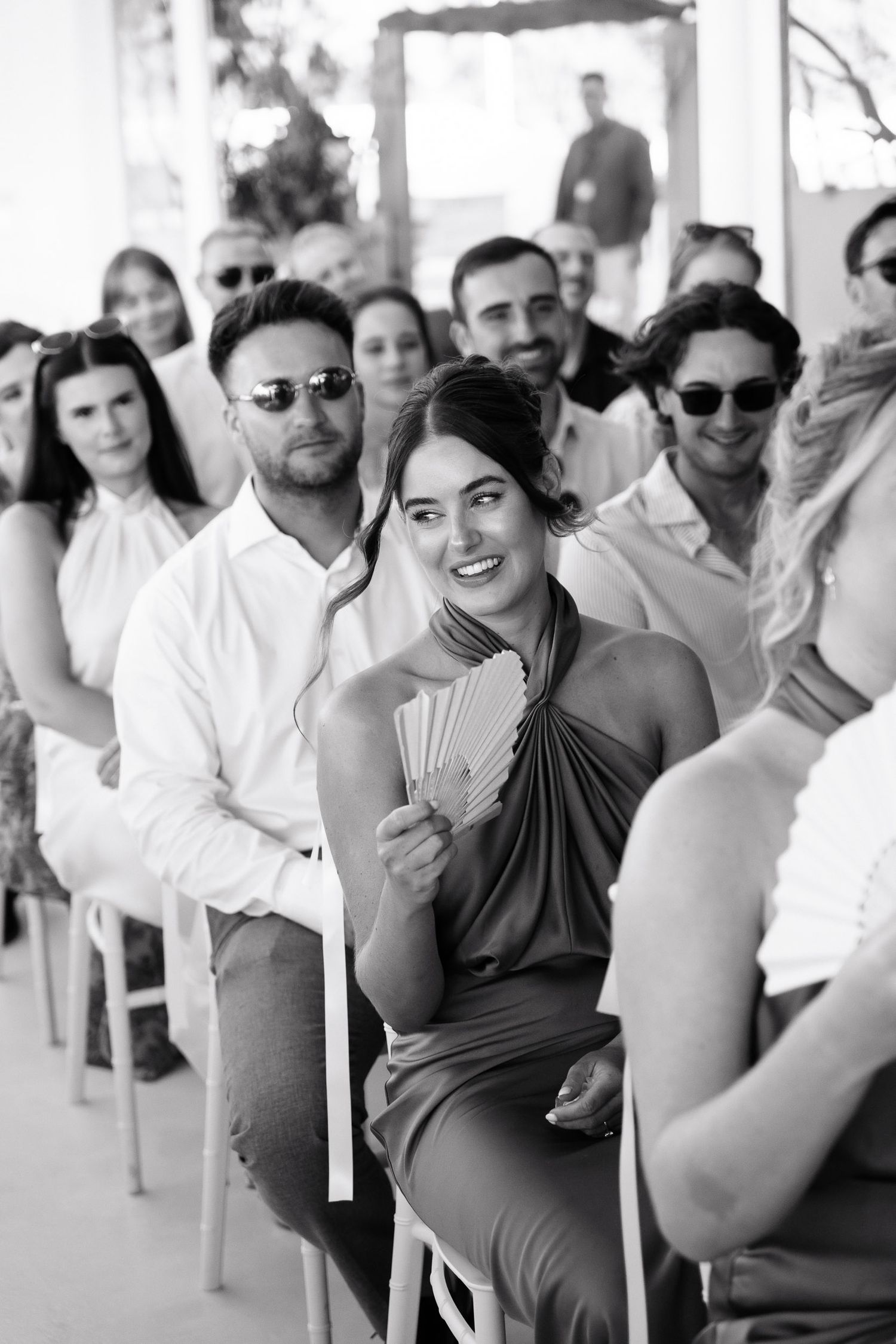 A group of people sitting in chairs outdoors at a casual gathering, wearing sunglasses and summer attire.