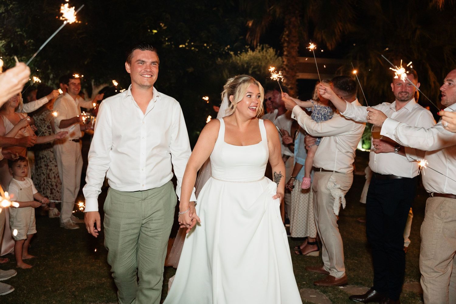 Wedding celebration at night with sparklers as newlyweds walk through guests holding lit sparklers on their special day.