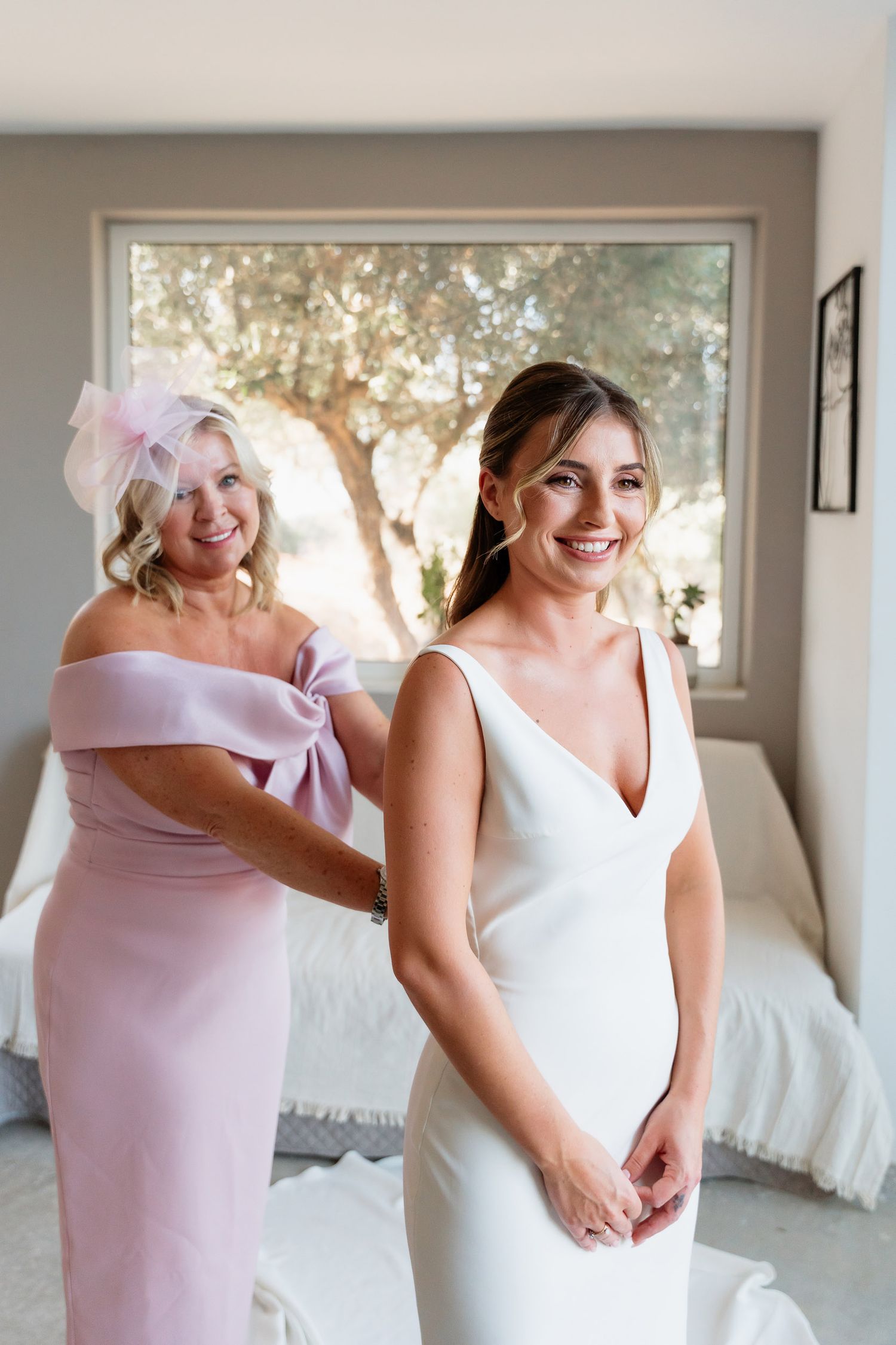Candid moments of bridesmaids in pink dresses helping with wedding preparations and sharing joyful embraces.