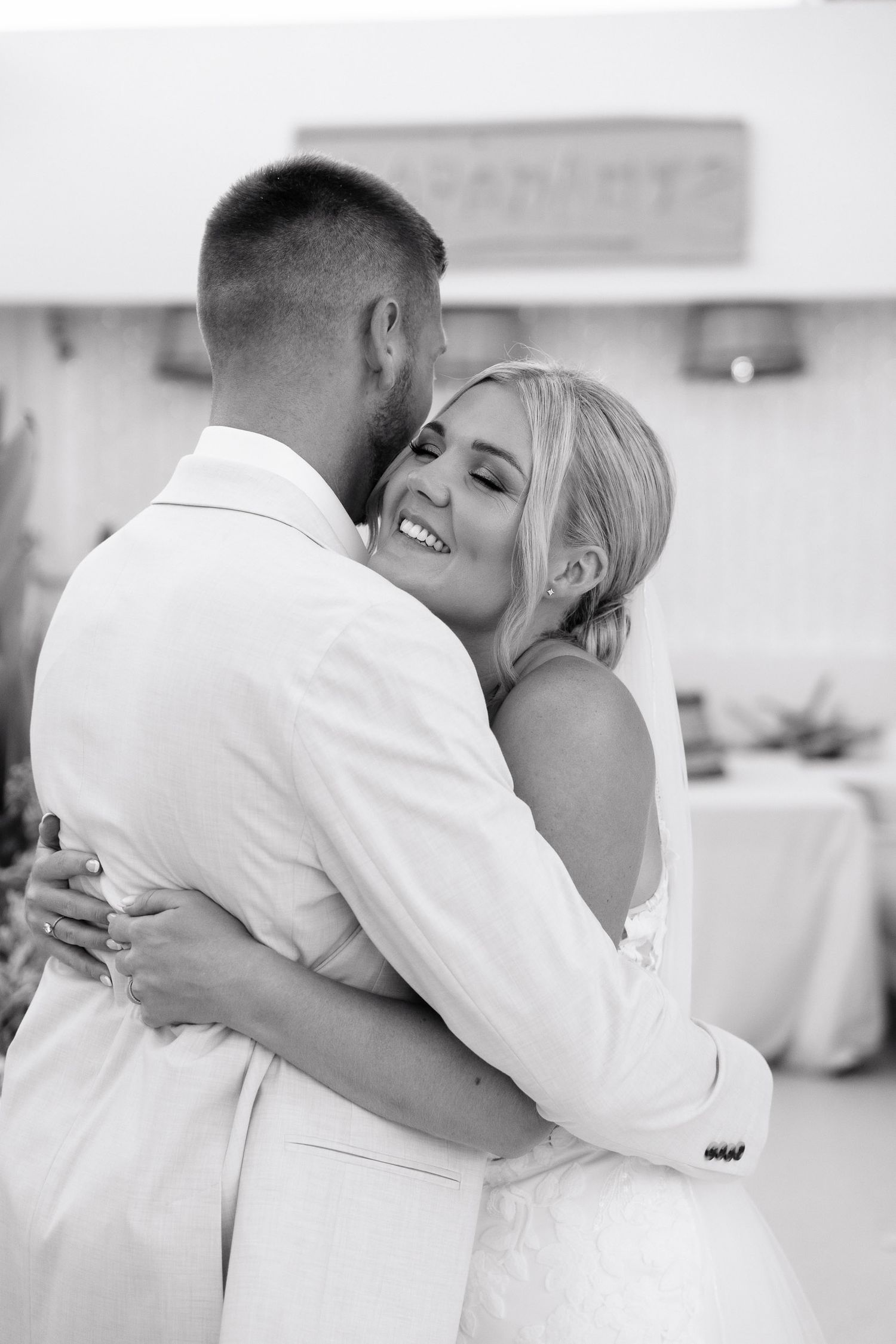 A black and white photo captures a tender moment between newlyweds sharing their first dance at their wedding reception.