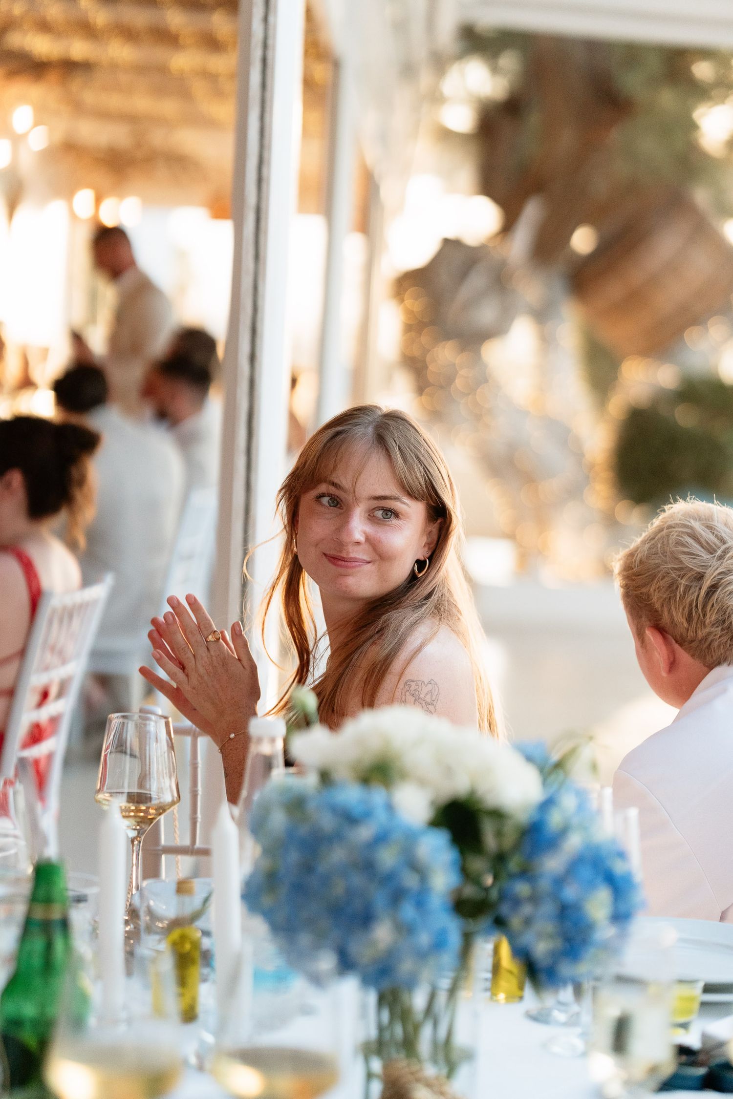 Wedding reception table decorated with blue hydrangea centerpieces and glassware in a bright sunlit venue.