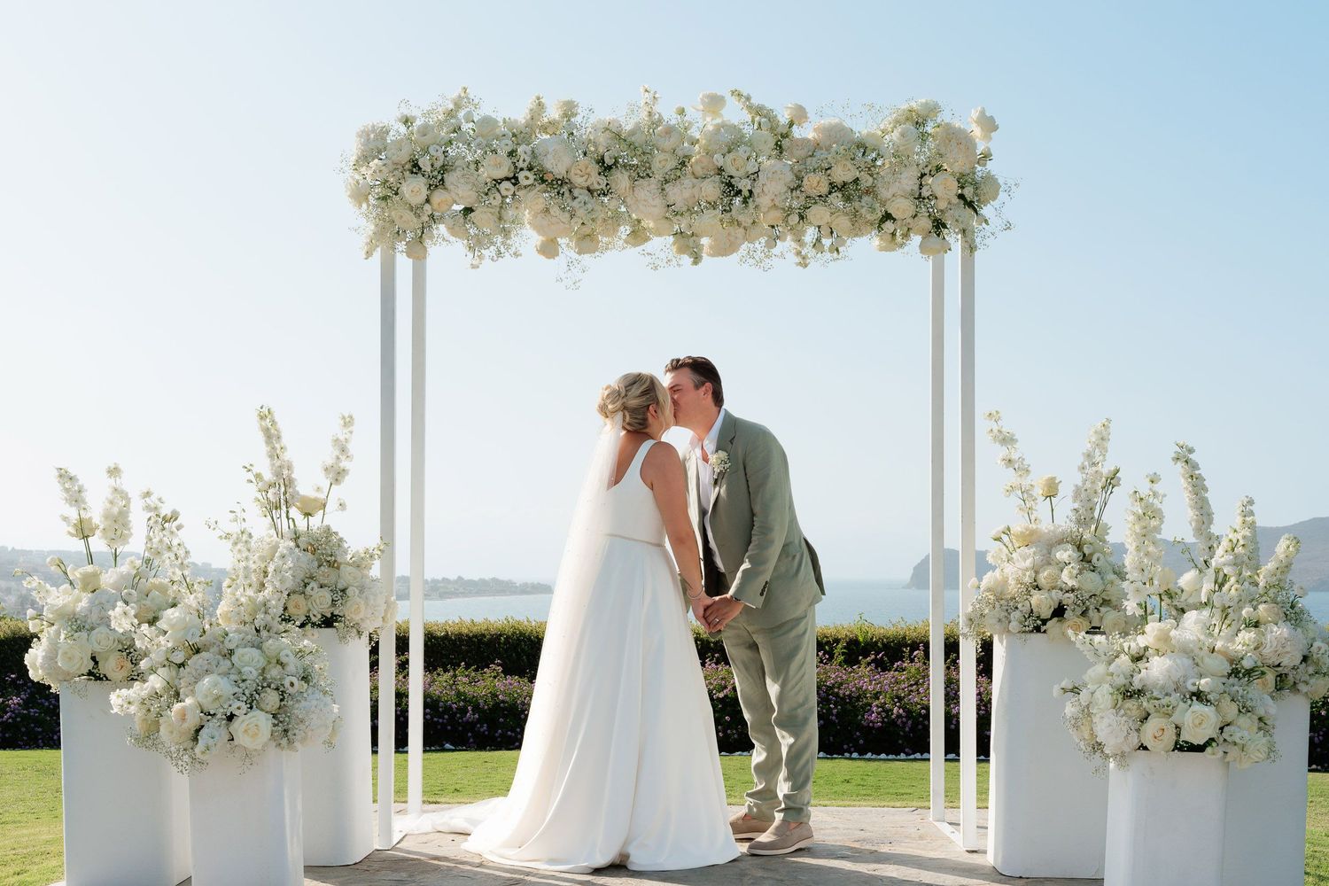 A romantic outdoor wedding ceremony setup with white floral arrangements and an elegant waterfront view.