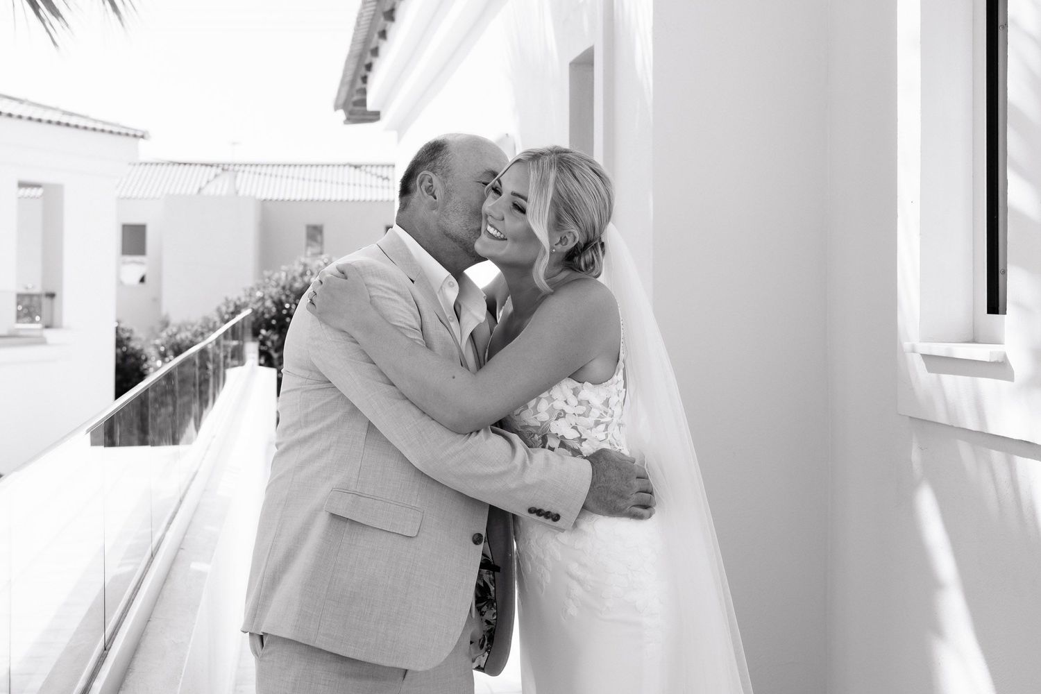A couple in wedding attire dance together in an elegant white room with natural light streaming through windows.