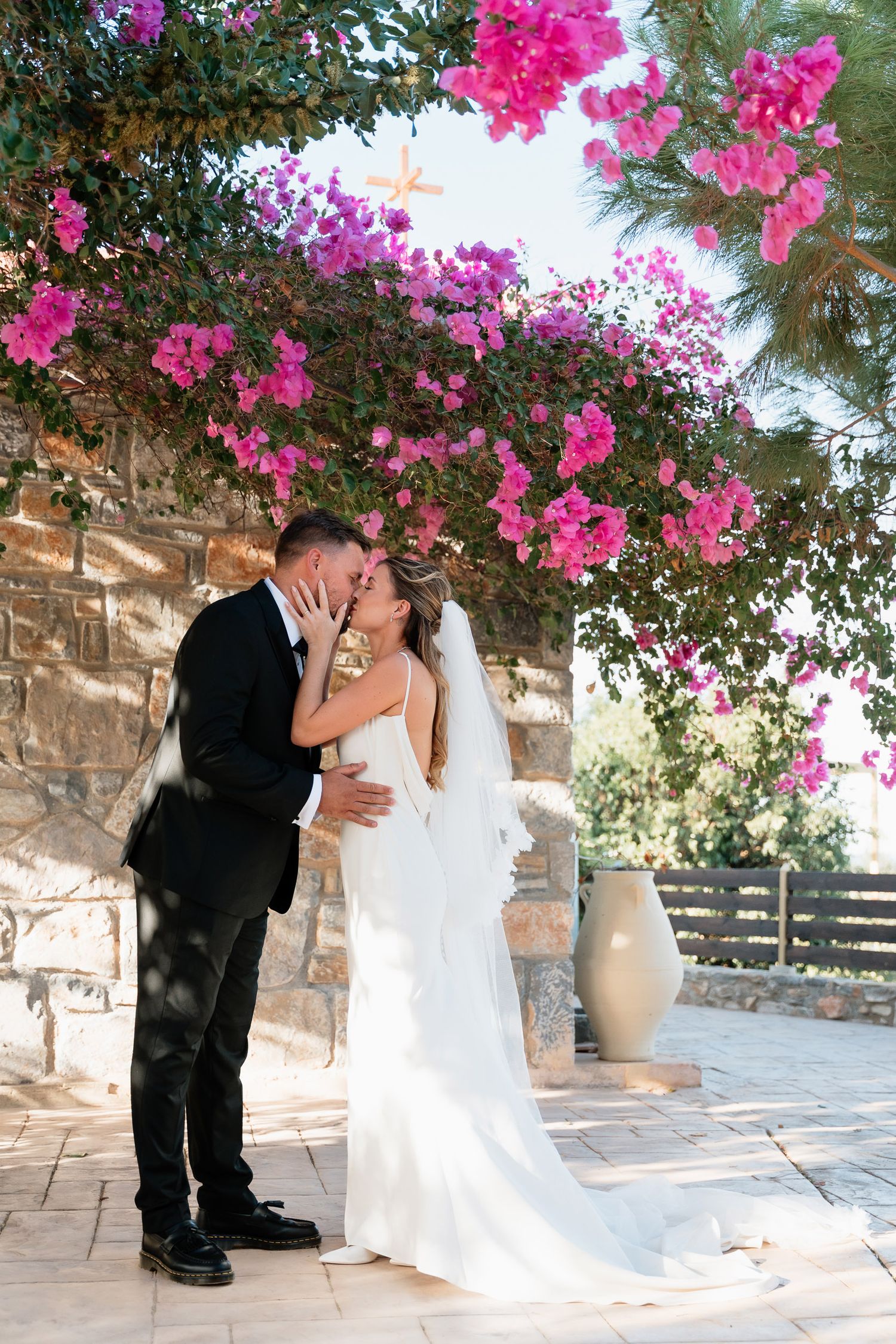 A romantic wedding sequence under vibrant pink bougainvillea flowers and stone walls on a sunny Mediterranean patio.