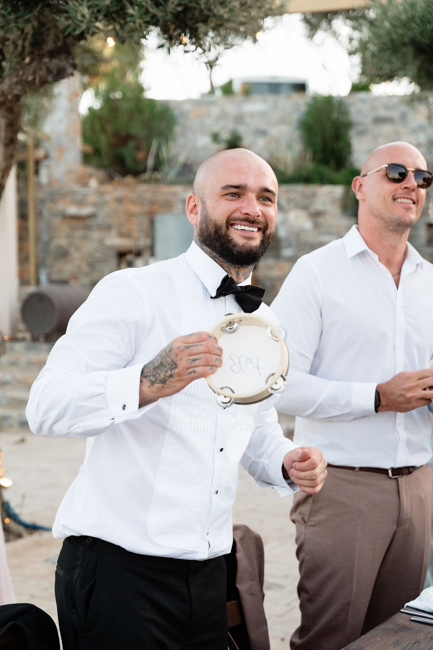 Musicians performing at an outdoor wedding celebration with a tambourine and white formal attire.