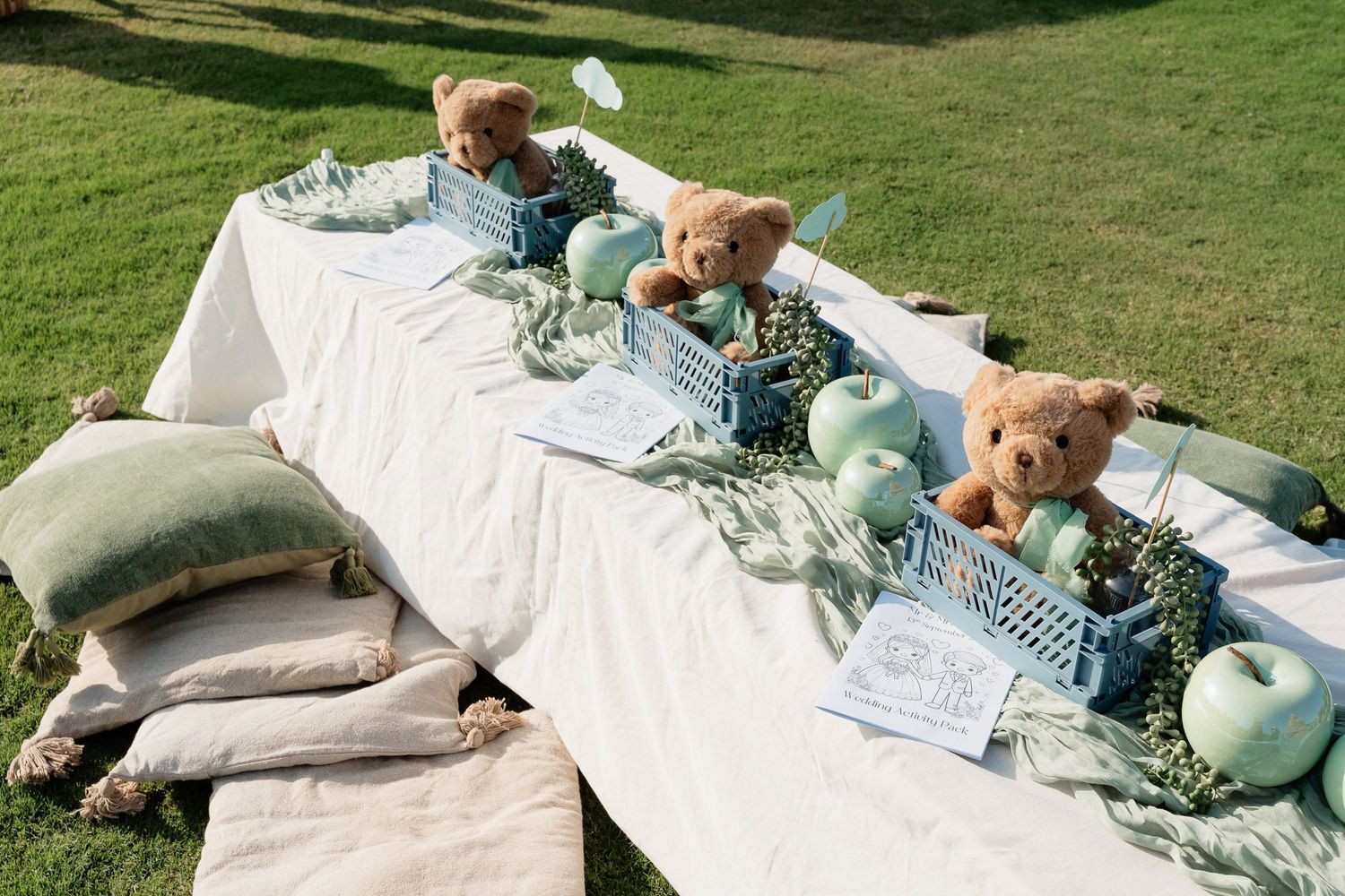 A rustic outdoor table setting with blue pumpkins, eucalyptus garland, and gray pillows on a white tablecloth.