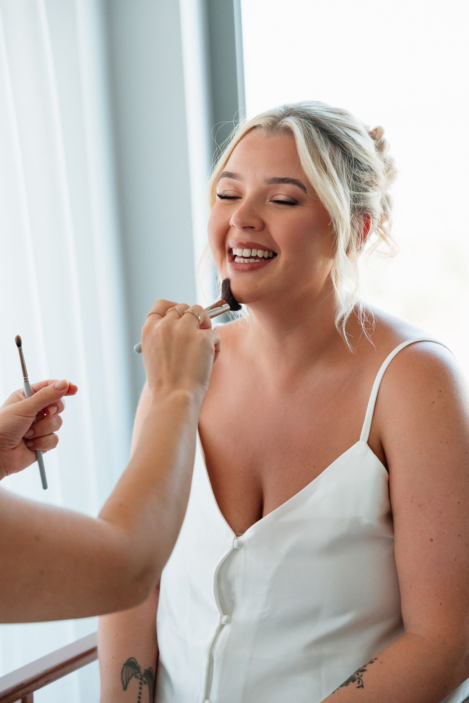 A series of four photos showing a person in a white top having makeup applied while smiling and laughing.