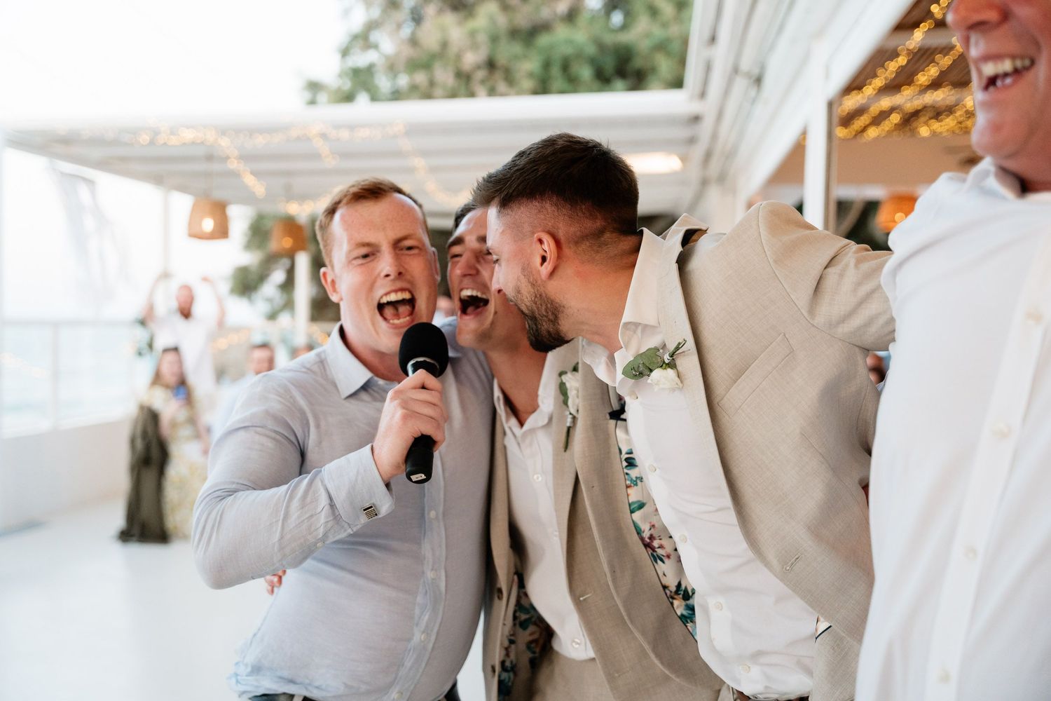 A group in formal attire laughs and smiles together during a wedding reception celebration.