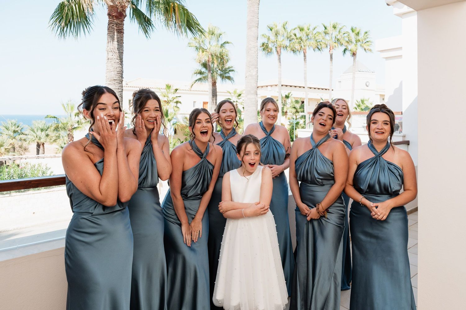 Bridesmaids in dusty blue dresses pose with bride in white gown at tropical beach wedding venue.