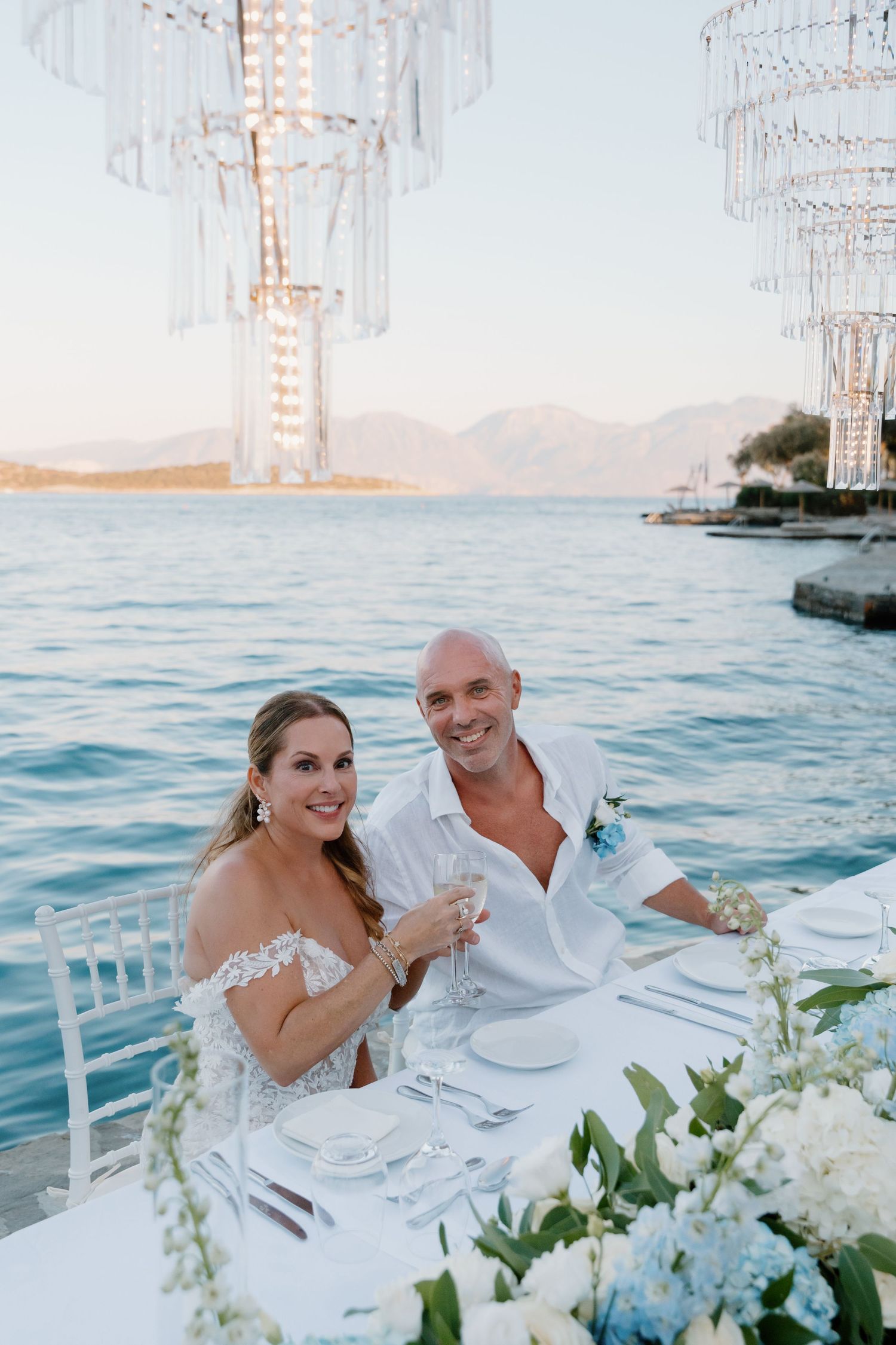 Waterfront wedding dinner setup with crystal chandeliers and ocean views at Minos Beach Art Hotel, Agios Nikolaos