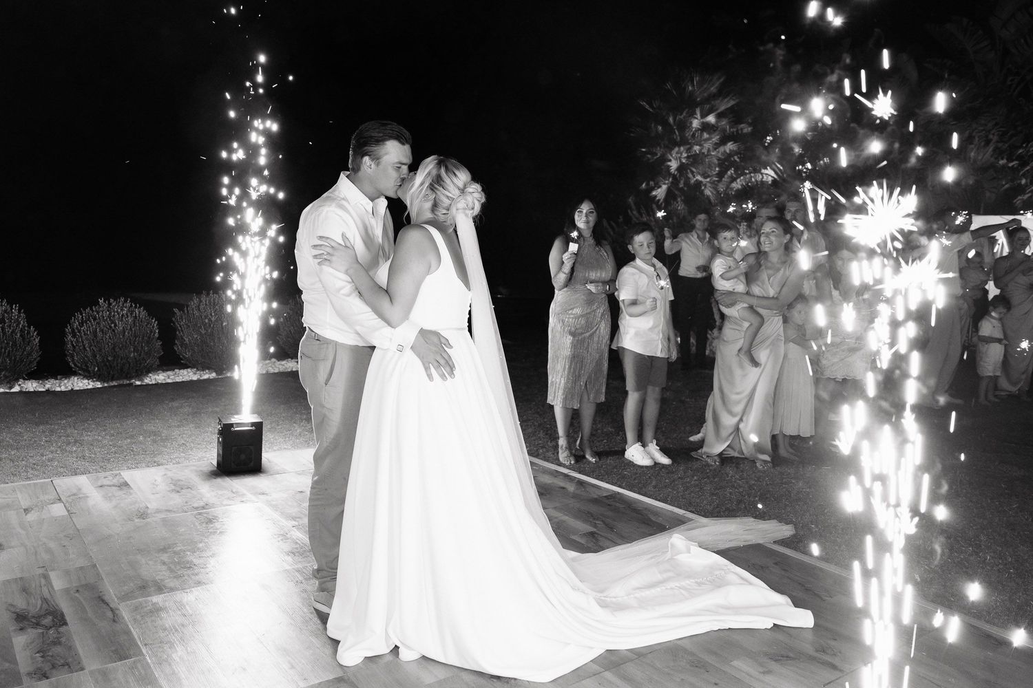 A couple shares their first dance at a nighttime wedding reception surrounded by sparklers and guests.