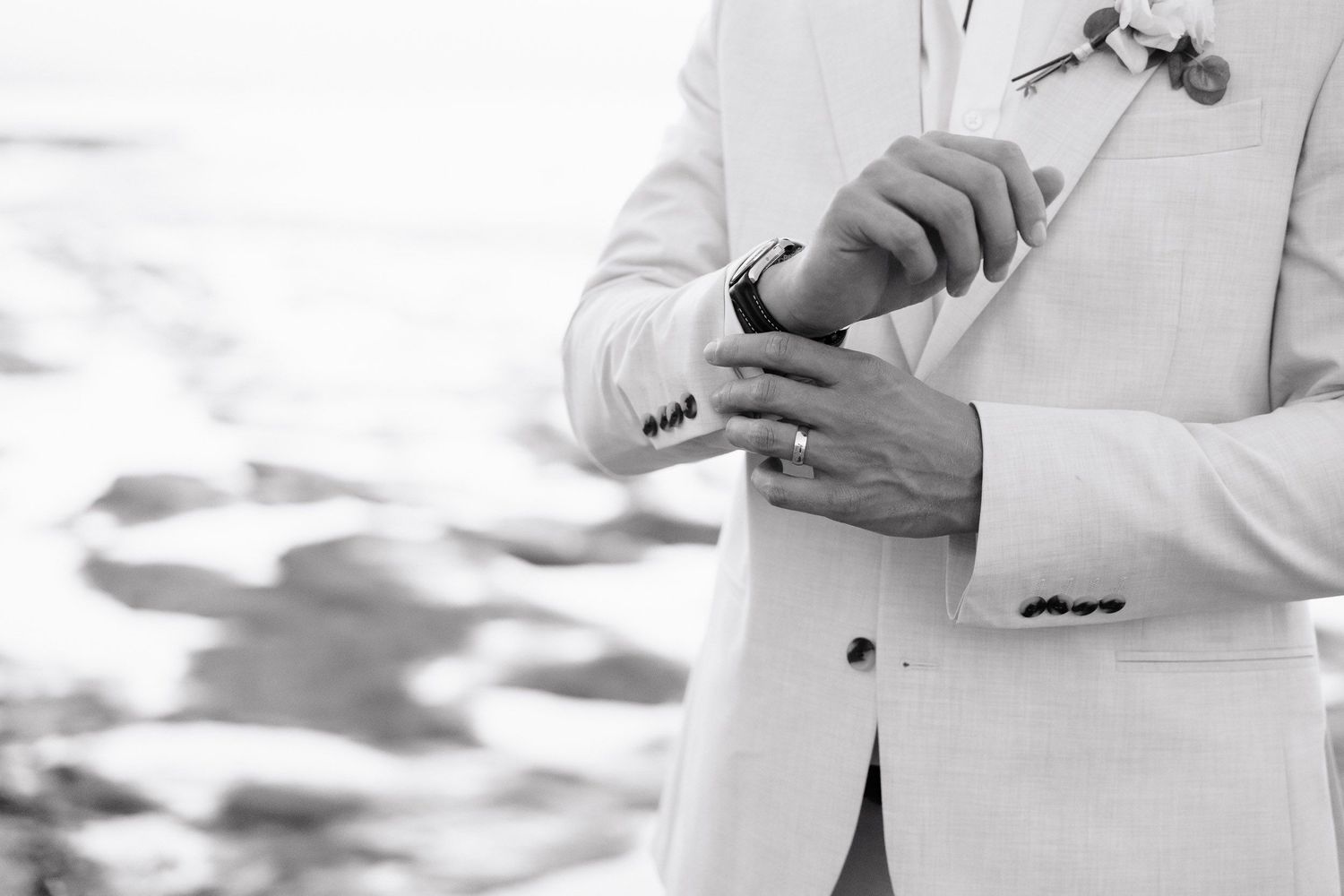 A person in a white suit jacket and dress shirt holds a glass of wine against a bright background.