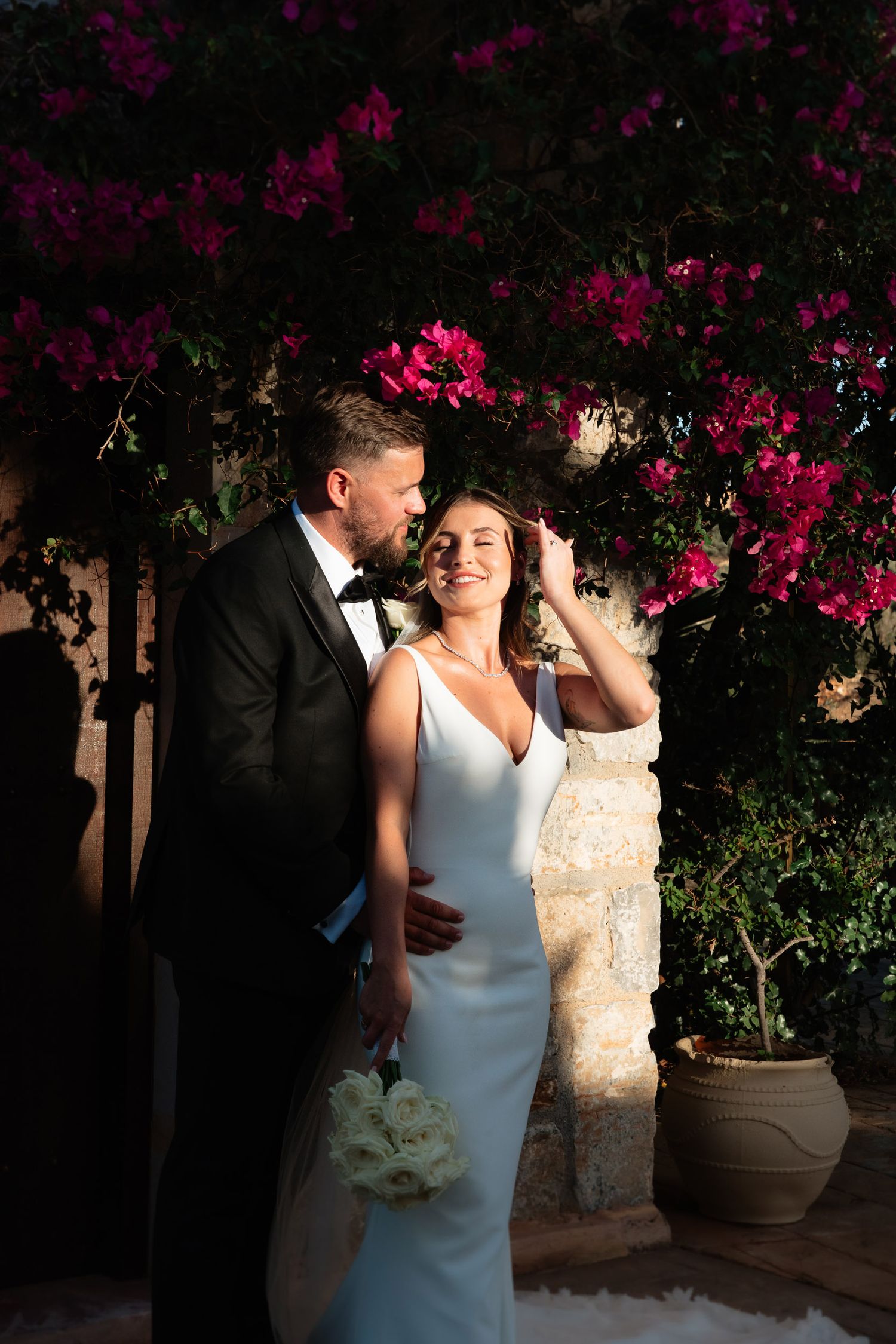 A romantic moment captured between newlyweds against a backdrop of vibrant pink bougainvillea flowers at dusk.