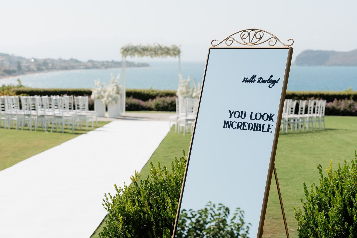 A scenic wedding venue setup with white chairs arranged on a lush green lawn overlooking a waterfront view.