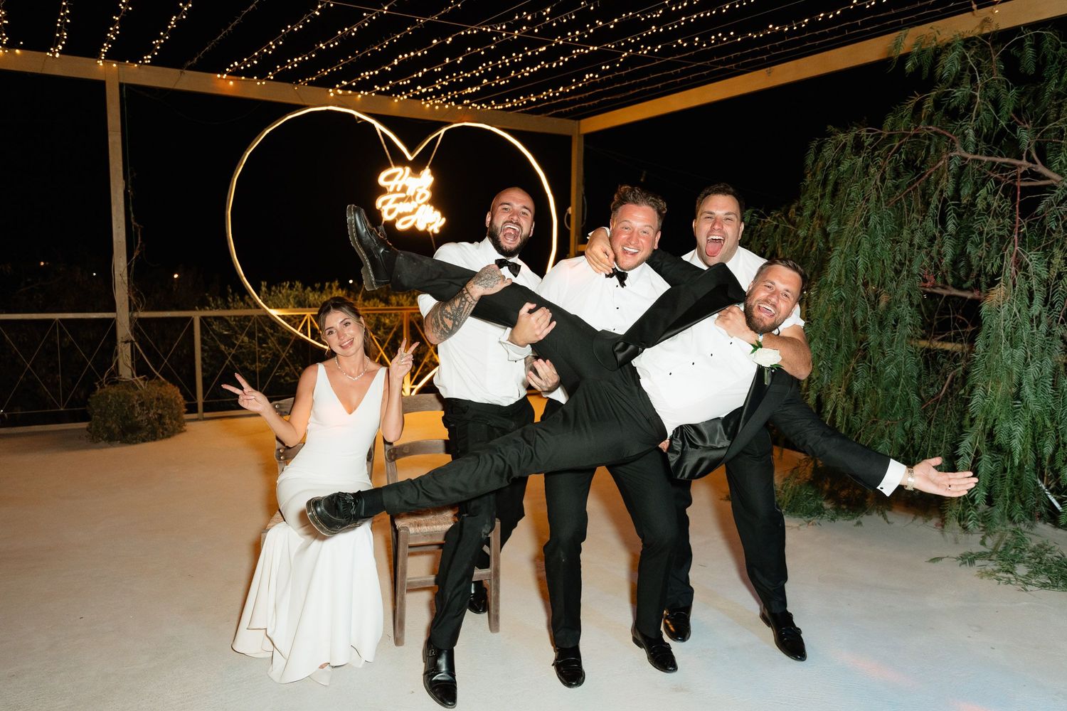 Wedding couple and guests perform coordinated dance moves in a line during an outdoor evening reception celebration.