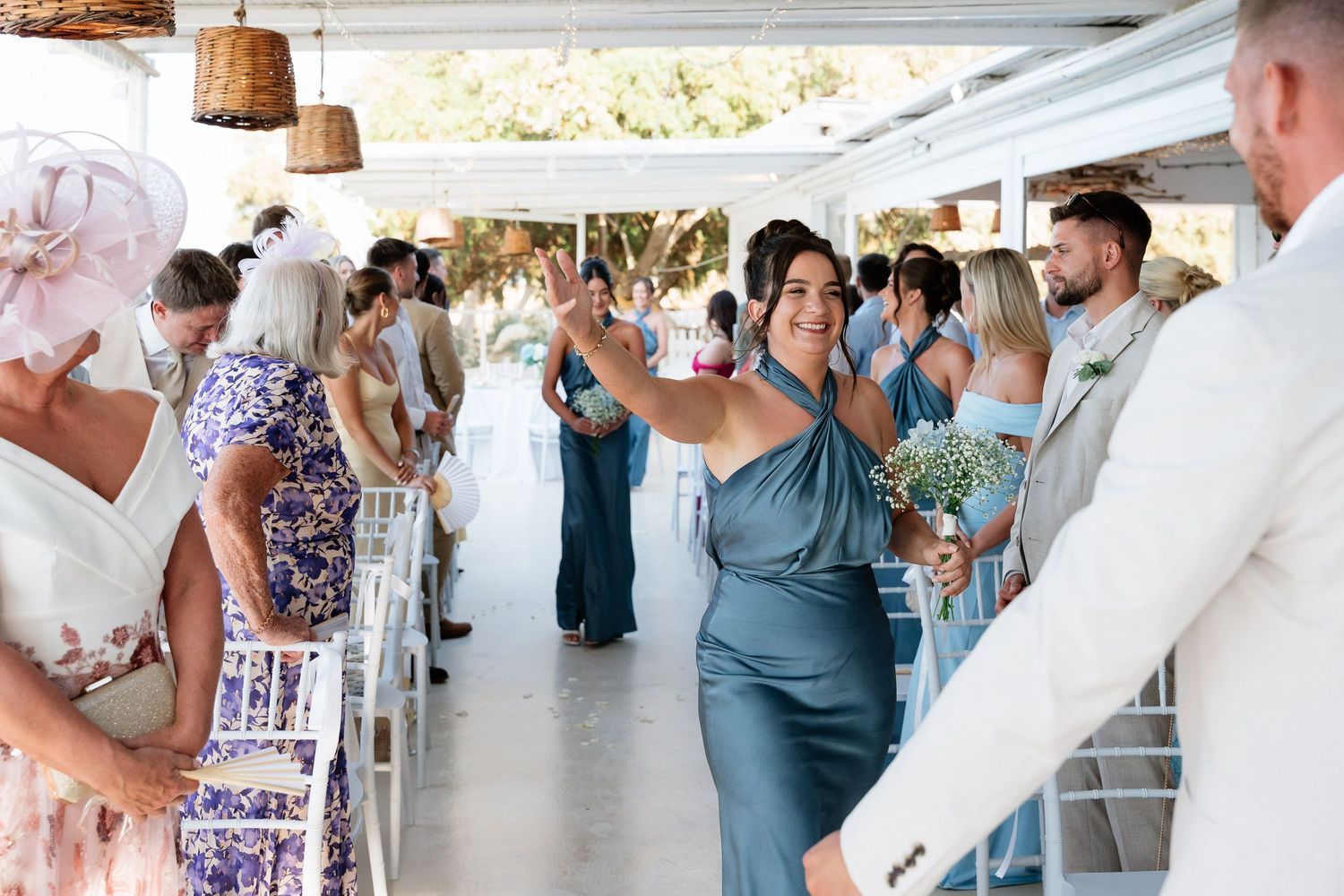 Wedding guests in blue dresses dance and celebrate during a reception at a bright indoor venue.