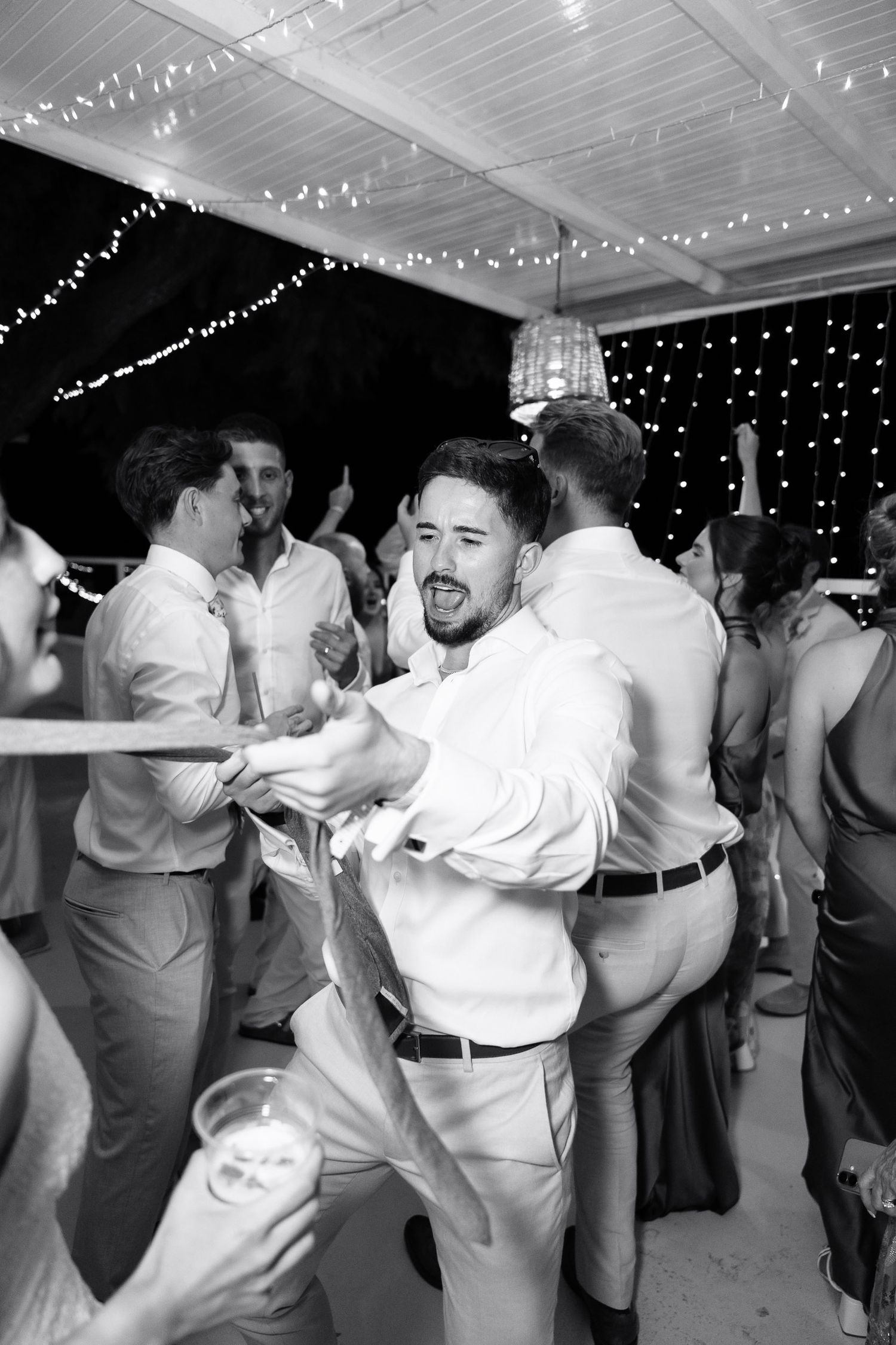 A sequence of black and white photos showing couples dancing together at a wedding reception under string lights.