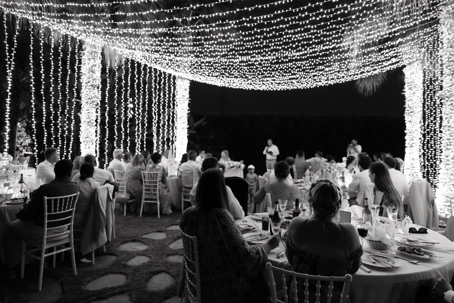 String lights create a magical canopy over an outdoor dining area at night creating an enchanting atmosphere.
