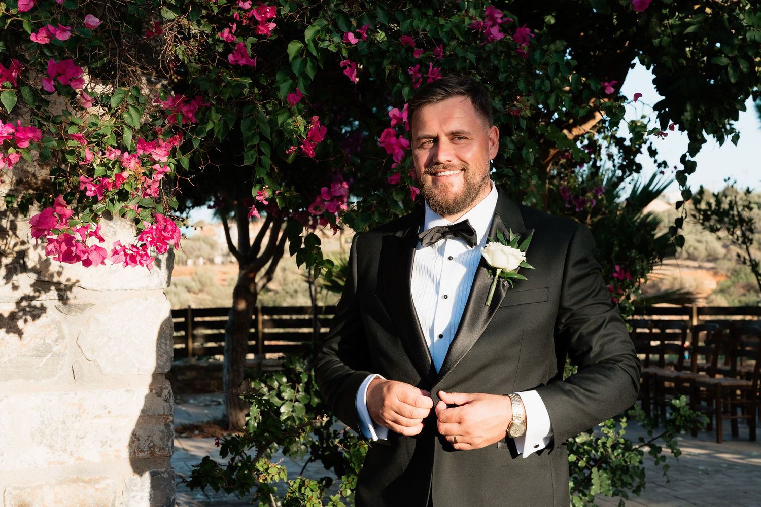A couple shares a romantic moment in a lush garden setting with pink bougainvillea flowers blooming overhead.
