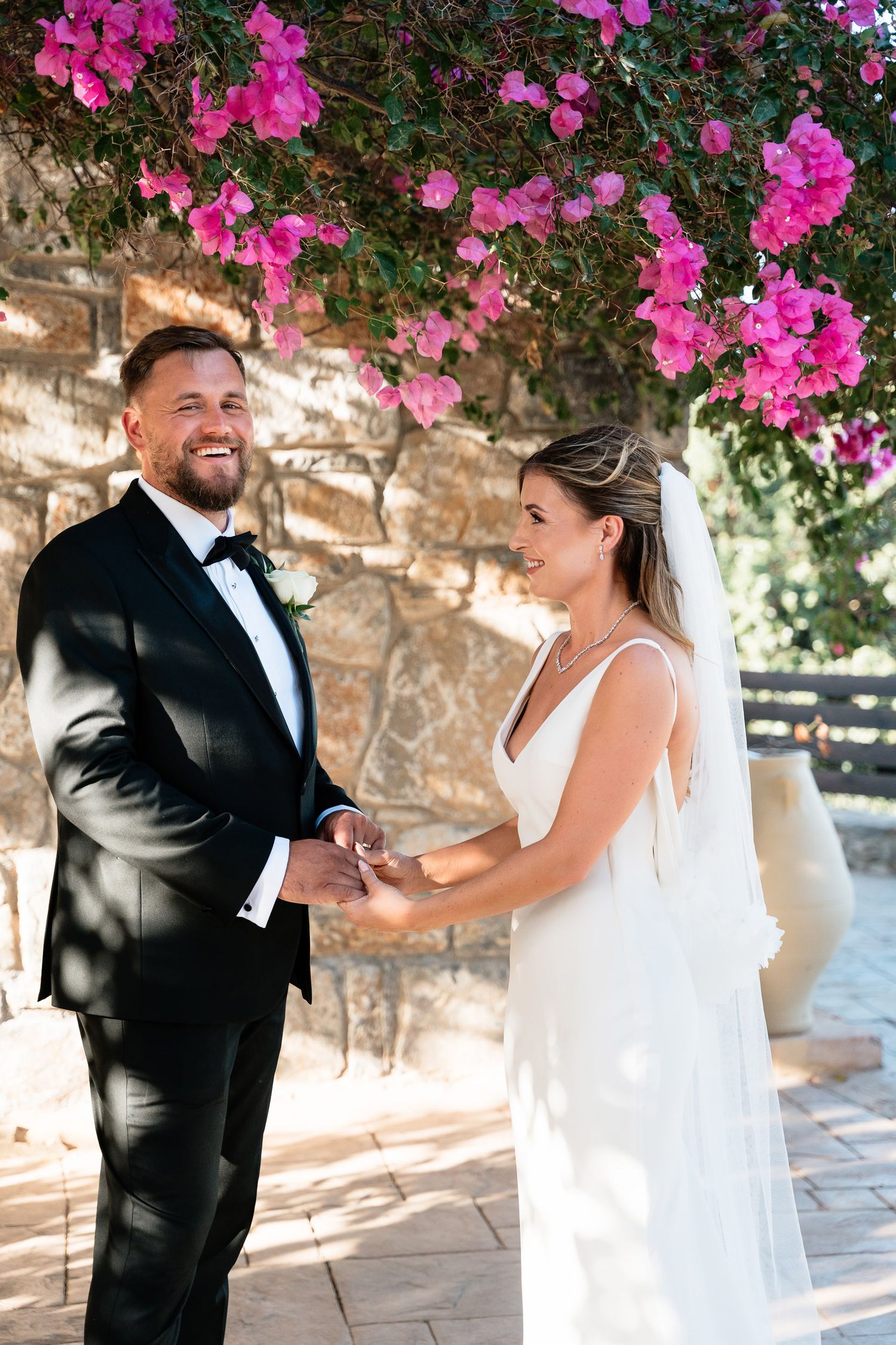 A joyful couple shares a candid moment together under vibrant pink bougainvillea flowers during their outdoor wedding ceremony.