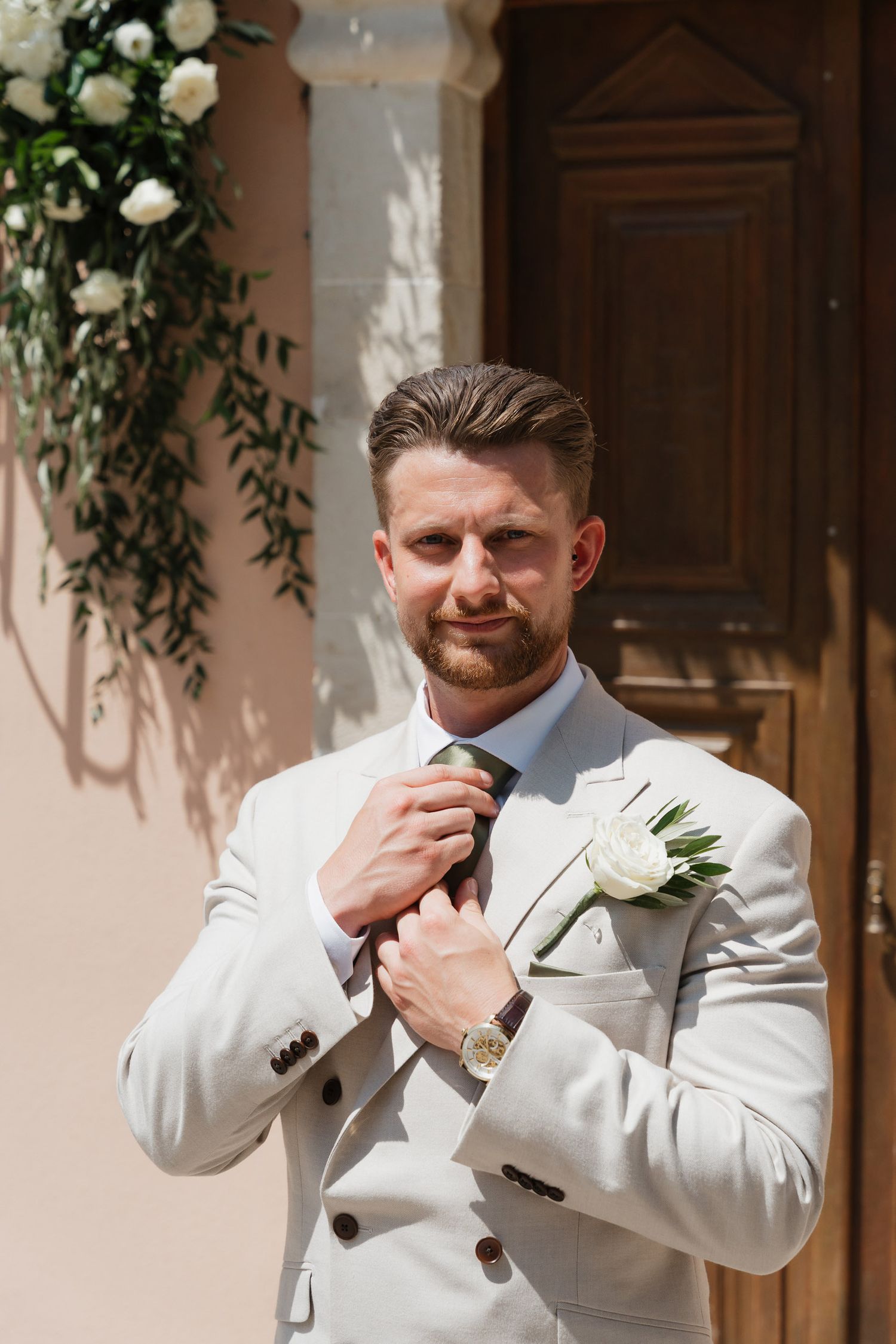 A series of four photos showing someone in a white suit jacket adjusting their boutonniere and cufflinks.
