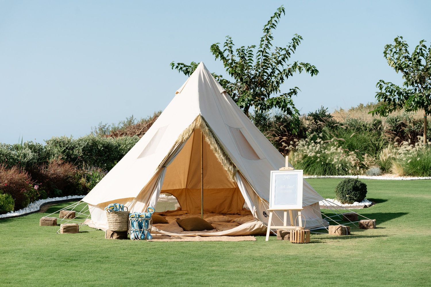 A luxurious white bell tent set up on manicured green lawn with outdoor furniture and decorative elements.