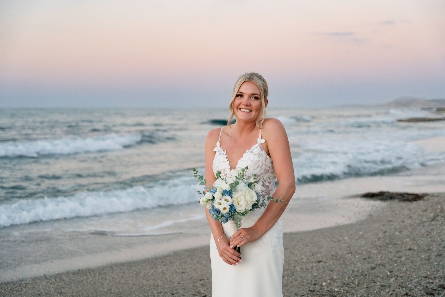 A beachside wedding photoshoot at sunset with soft pastel colors reflecting off the ocean waves.