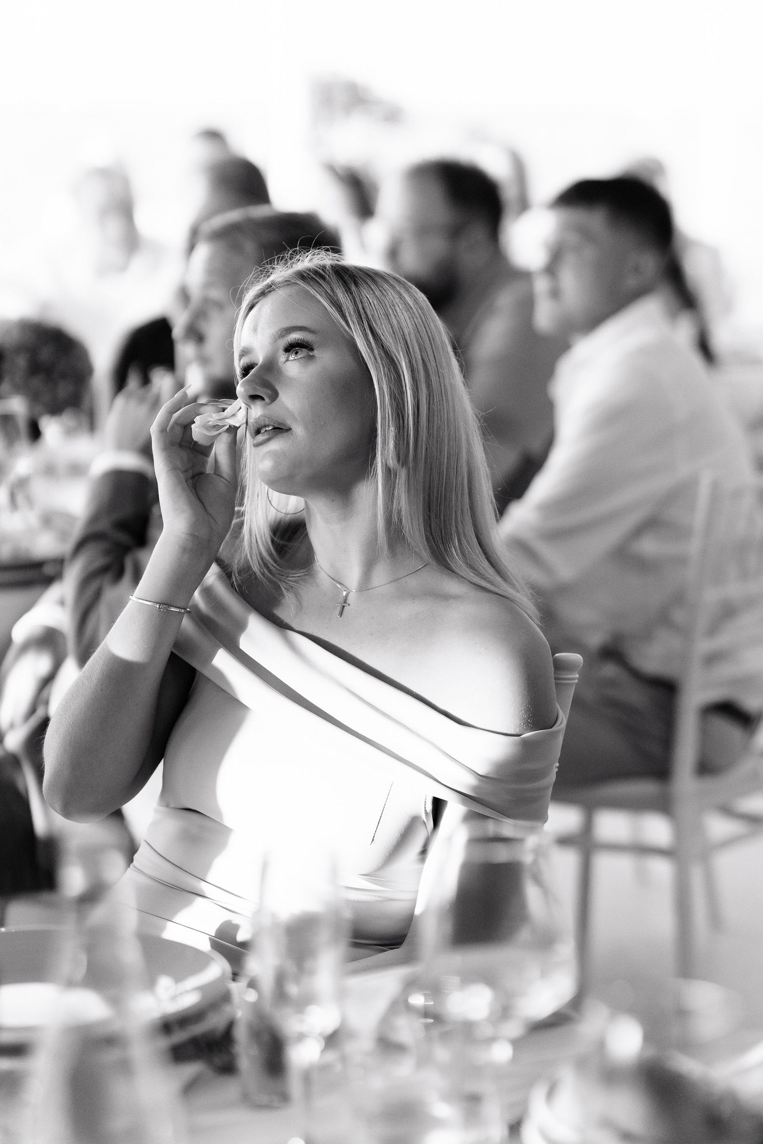 A black and white photo of an elegant guest in an off-shoulder dress at a formal dinner event.