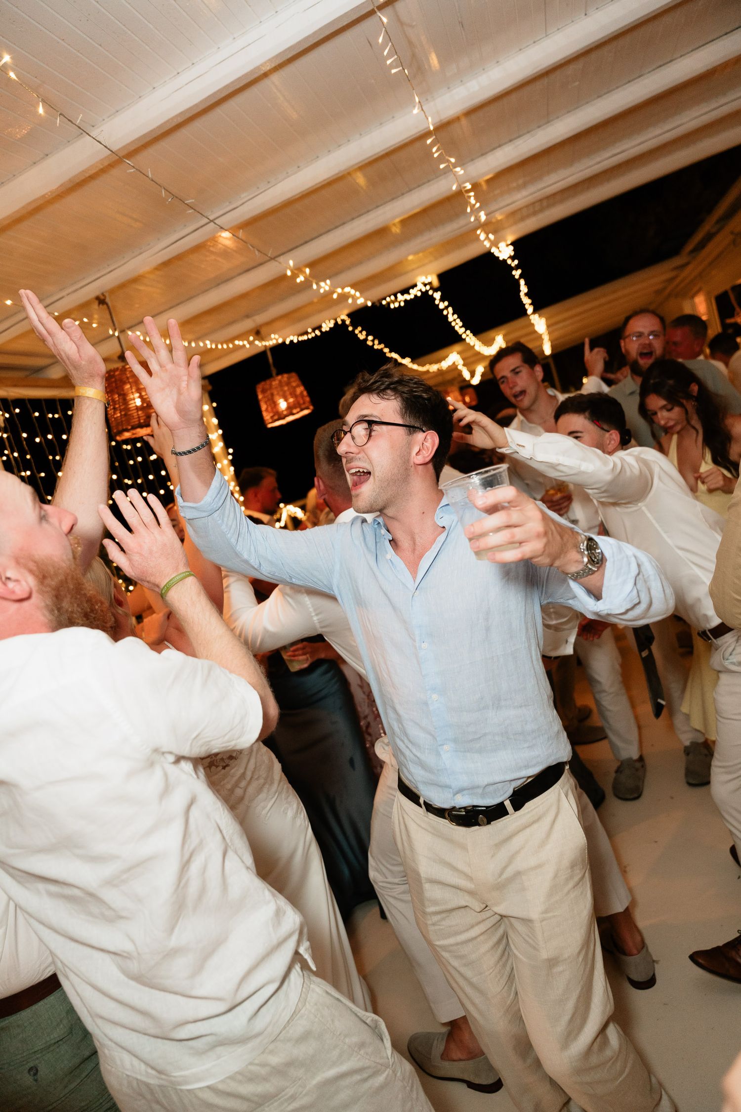 Party guests dance enthusiastically under string lights at an indoor celebration with a festive atmosphere.
