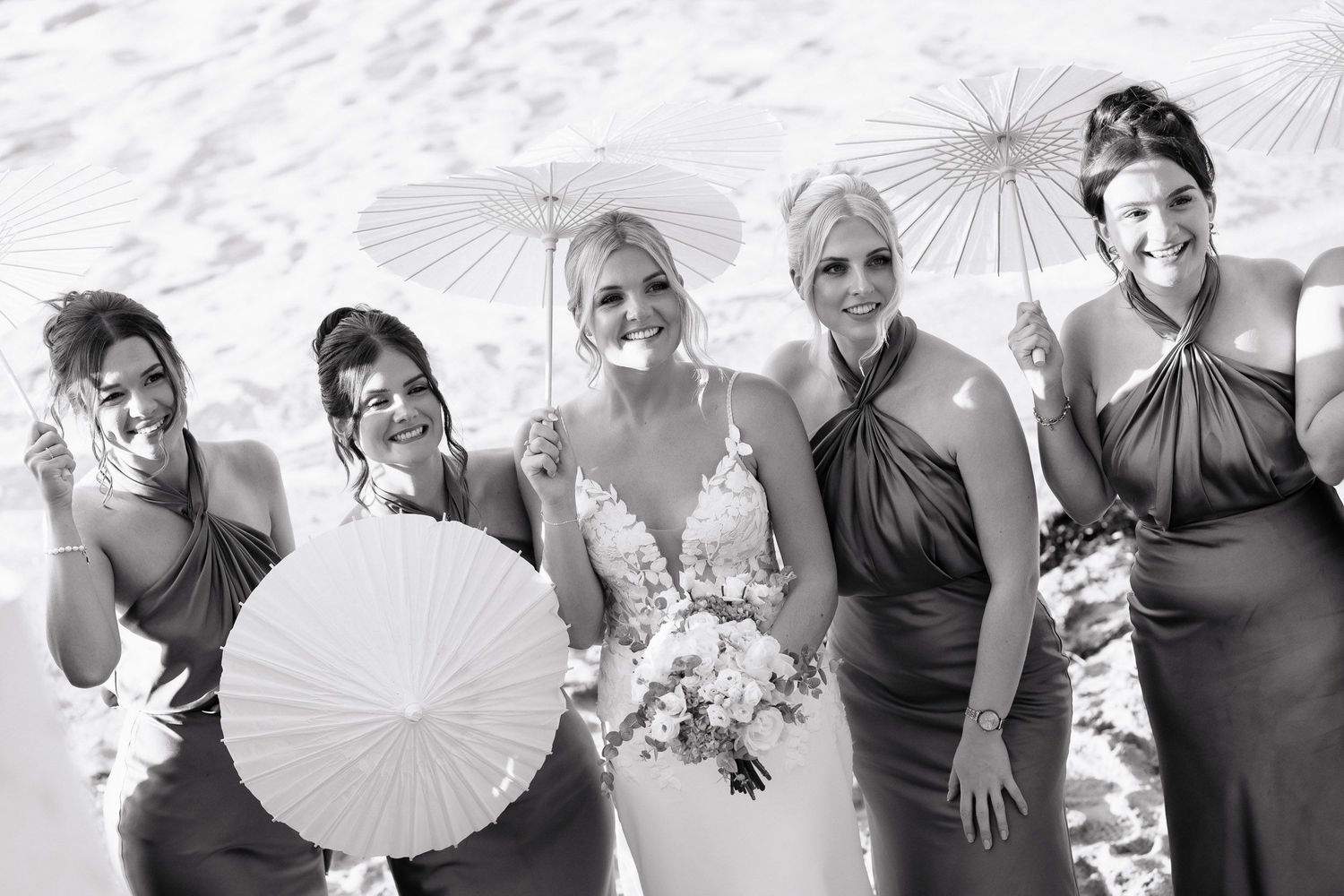 A series of black and white wedding party photos arranged horizontally showing people posing with white parasols.