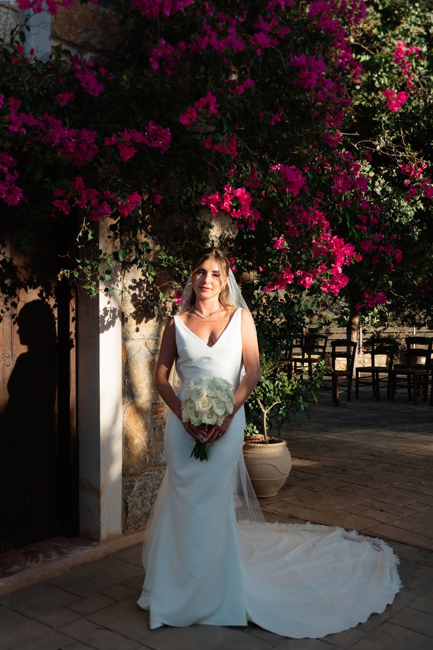 A bride in a white wedding dress poses under vibrant pink bougainvillea flowers during a romantic outdoor photo session.