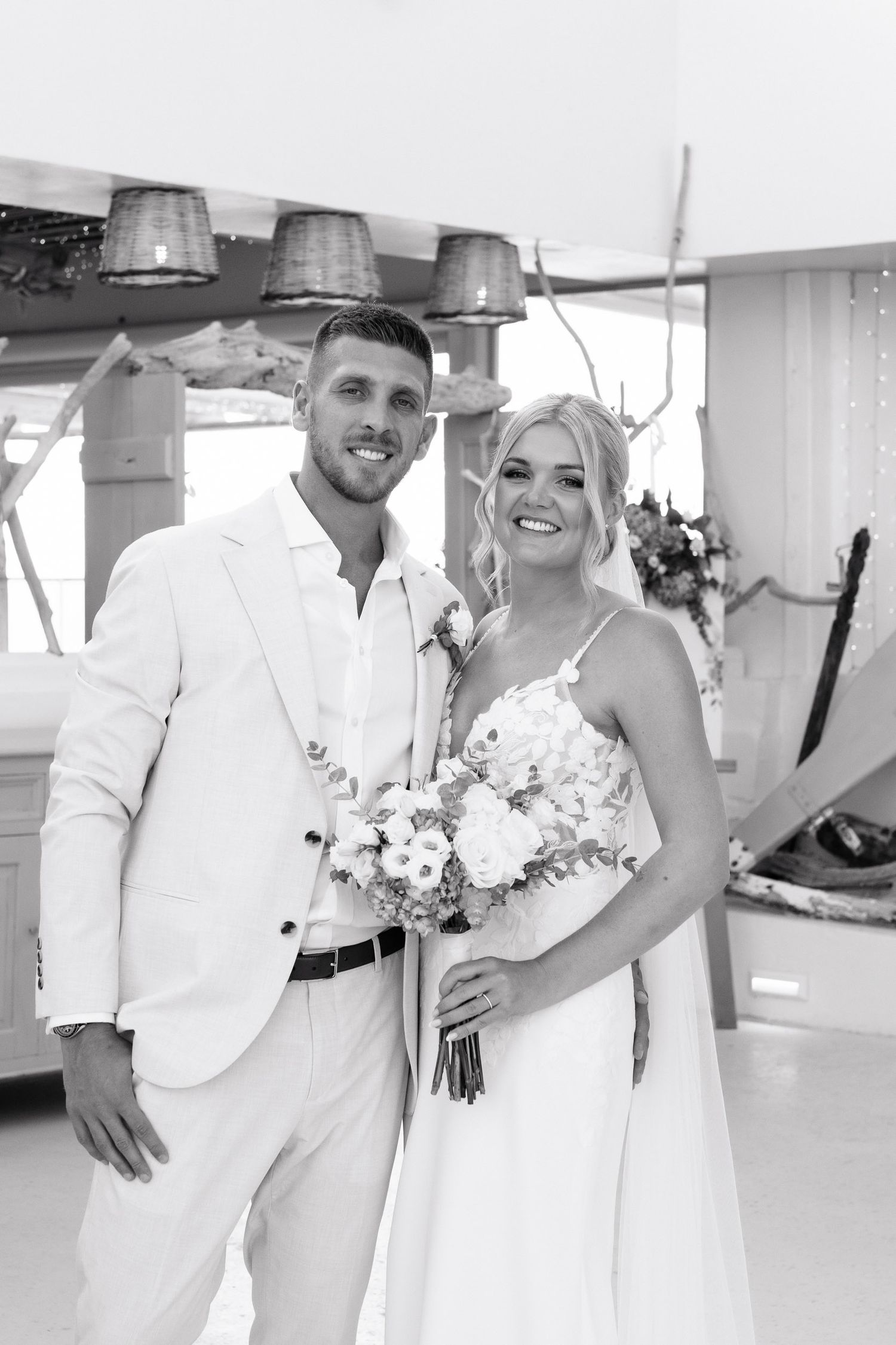 A black and white wedding photo series showing joyful moments between a couple in white attire and floral bouquets.