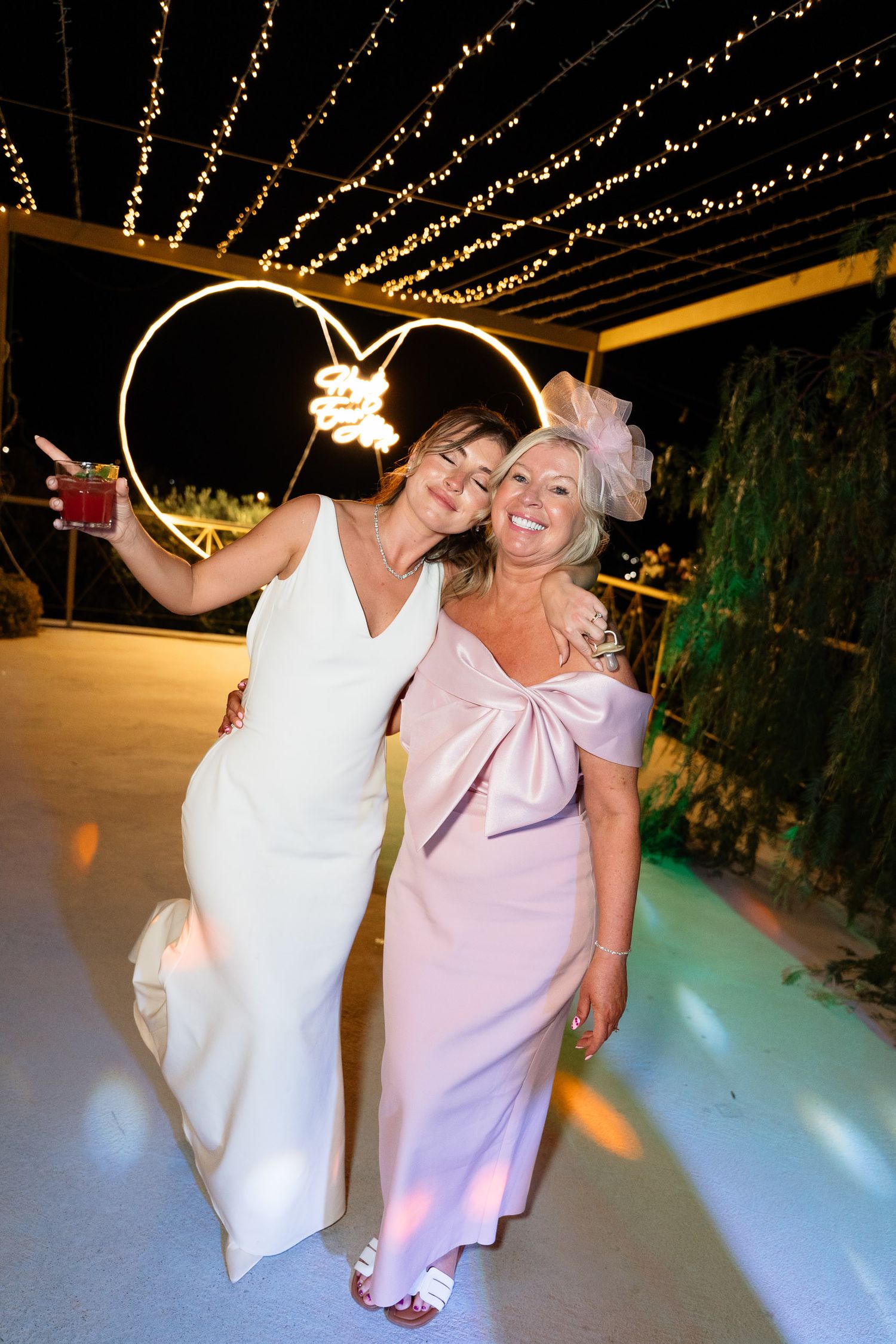 Two people dancing and laughing together on a white dance floor under decorative string lights at an evening event.