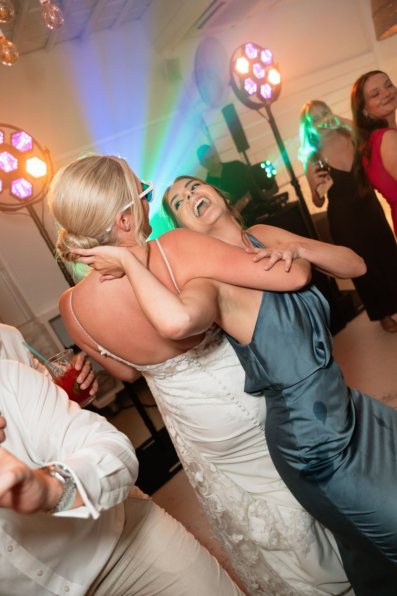 Wedding guests dancing energetically on a dance floor with colorful party lights illuminating the celebration.