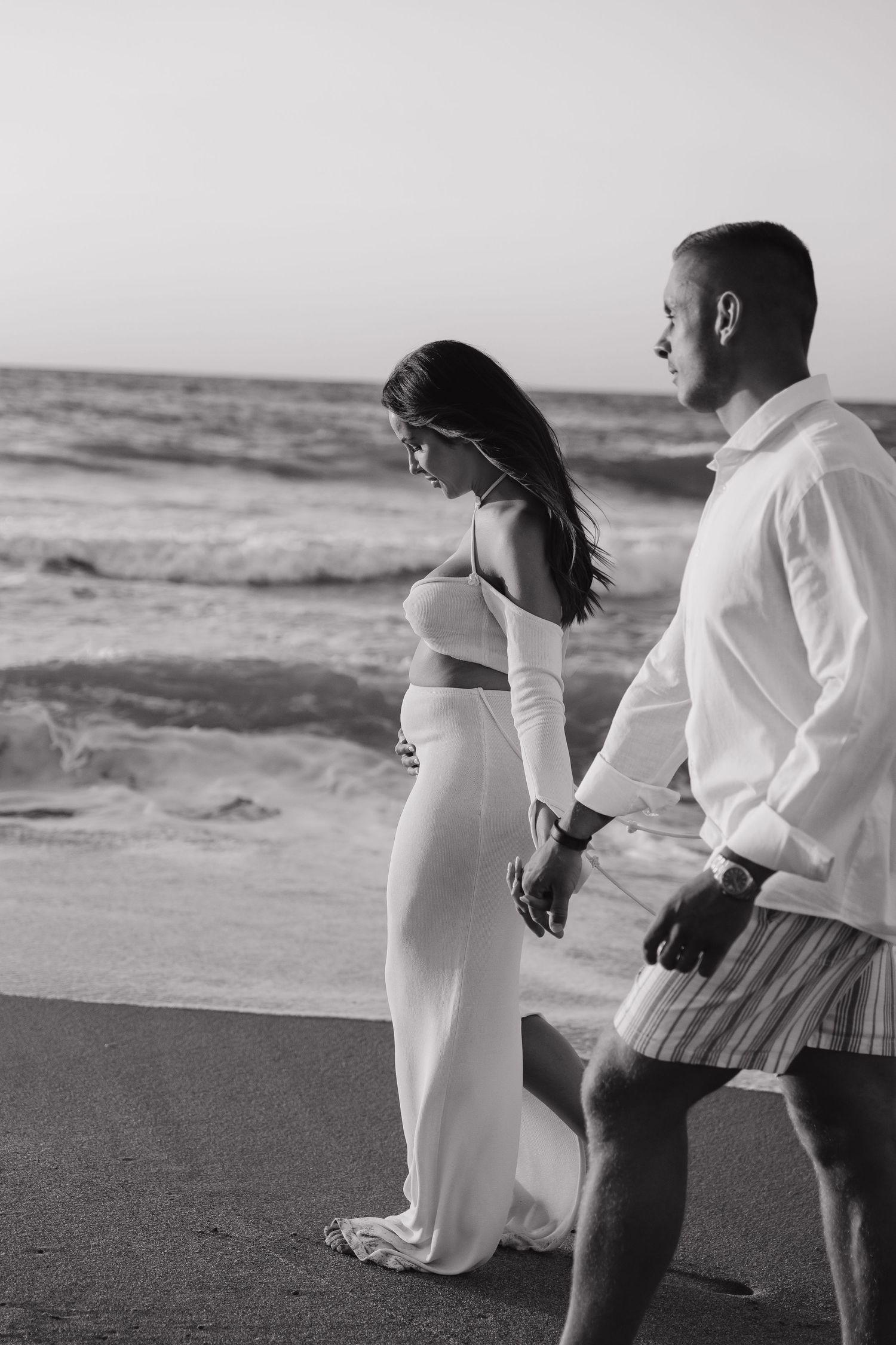 Black and white photo sequence of a couple walking hand in hand along a beach shore in formal attire.