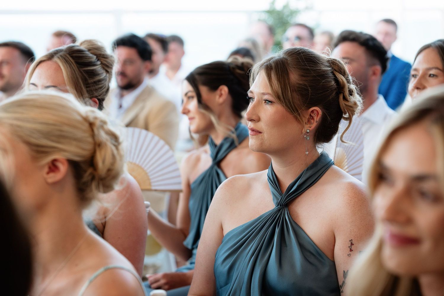 A crowd of wedding guests sitting in white chairs during an outdoor ceremony with palm trees in the background.