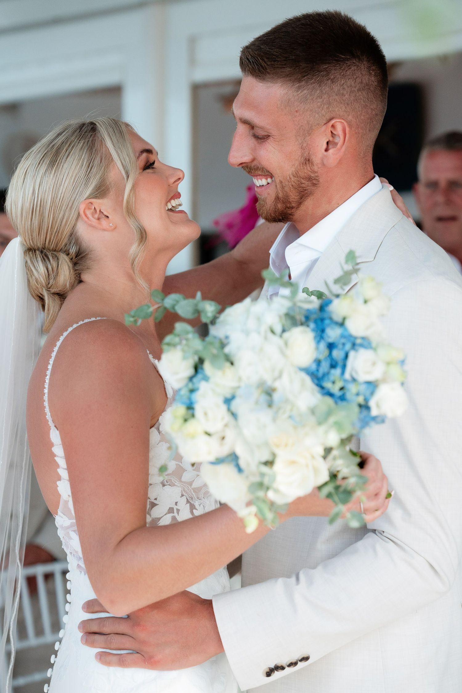 A joyful wedding couple shares a laugh while holding a beautiful blue and white floral bouquet.