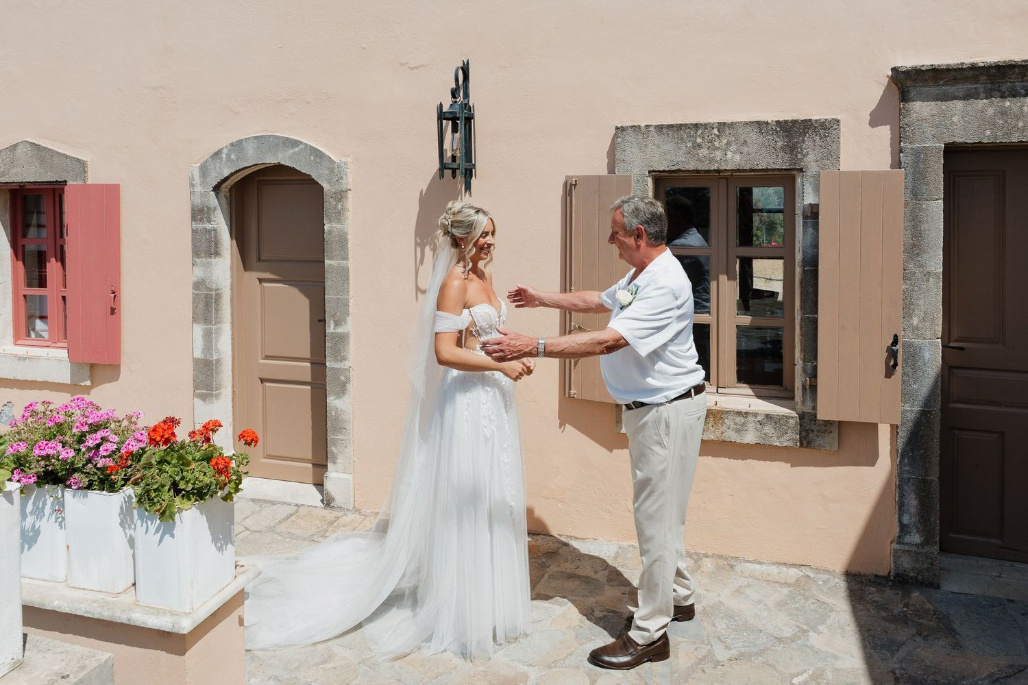 A romantic moment between two people in formal attire standing on a Mediterranean-style patio with pink flowers.