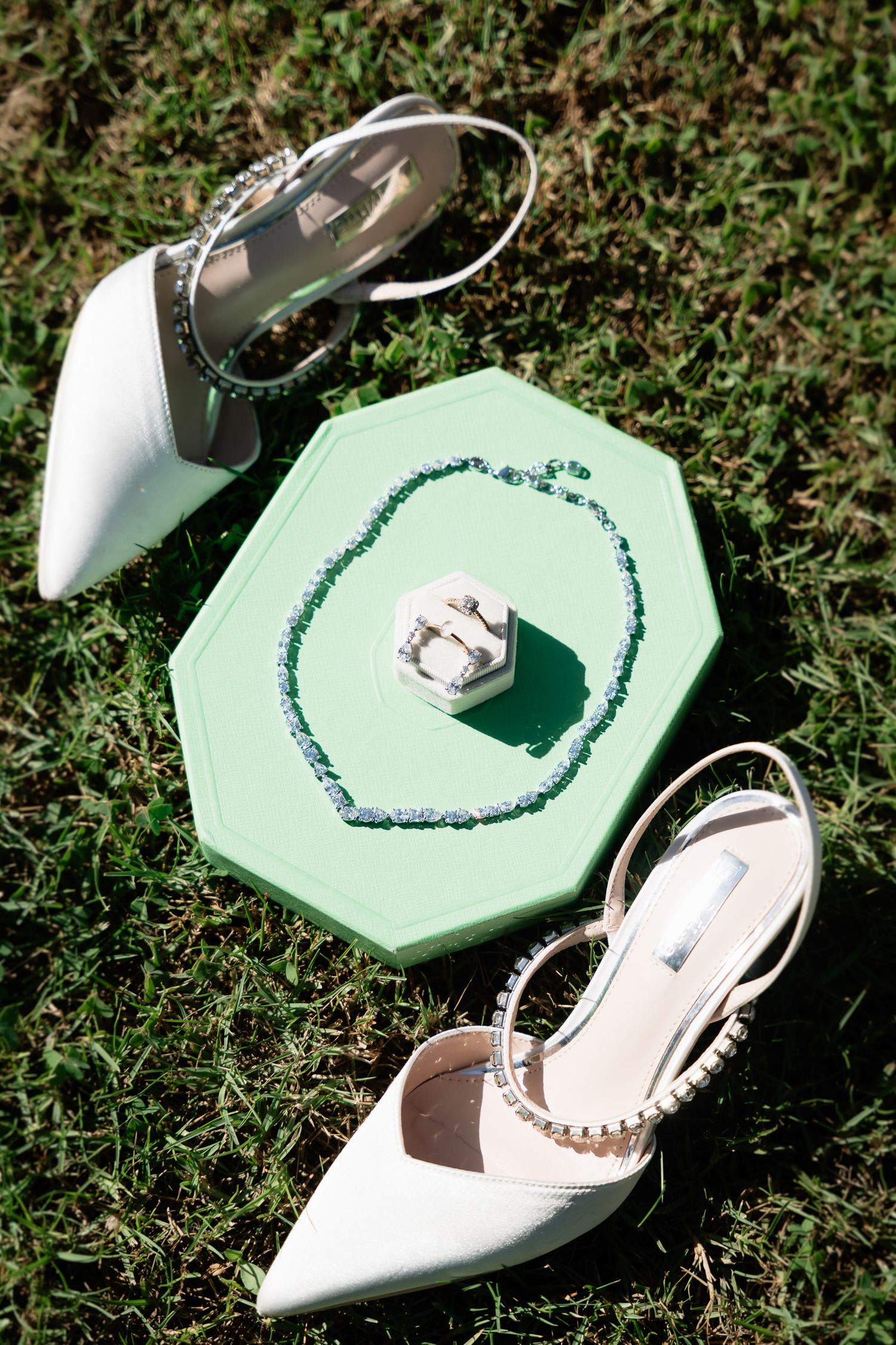 A series of photos showing a mint green hexagonal ring box with white satin heels on grass.