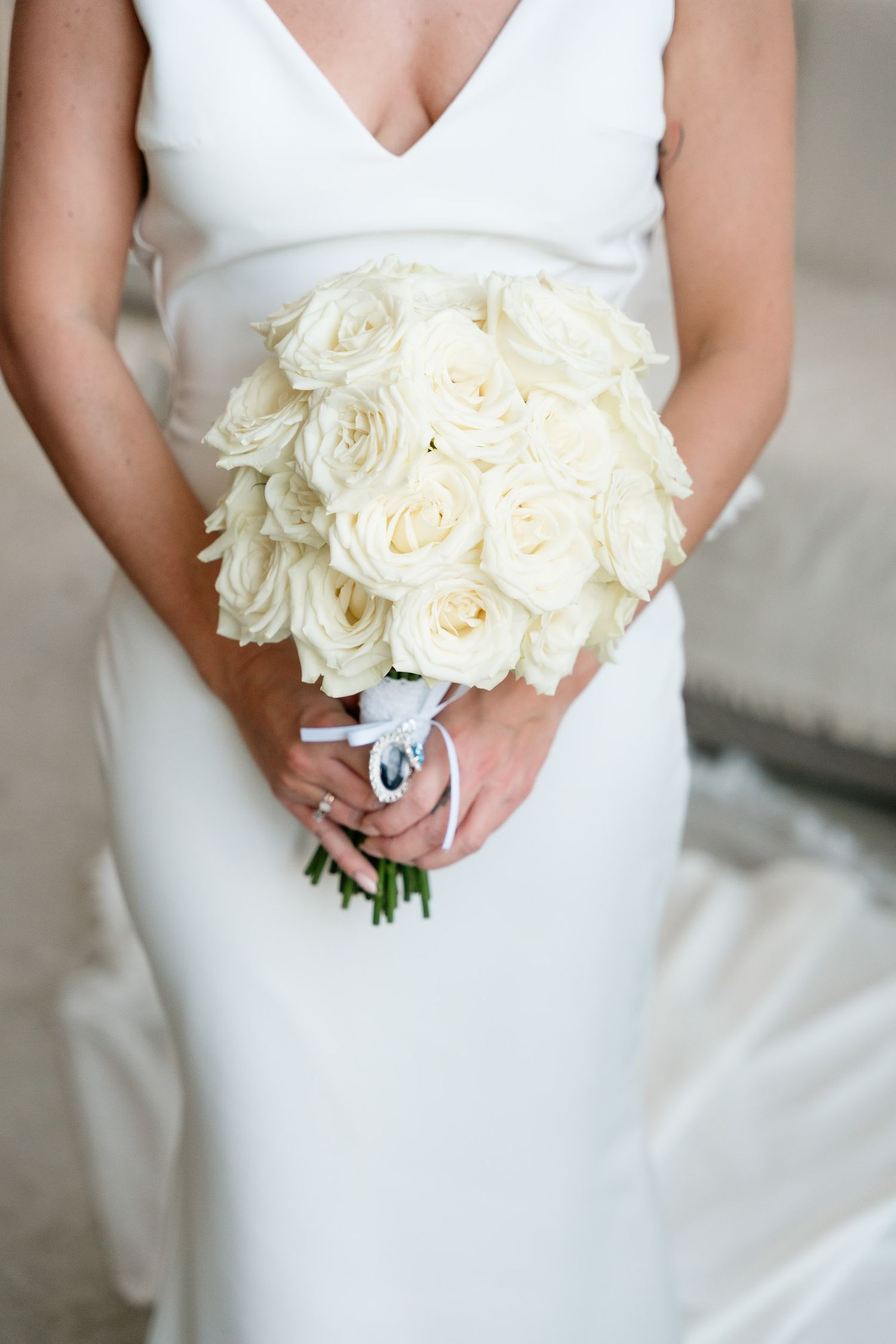 A classic white rose bridal bouquet held against an elegant white wedding dress in a close-up shot.