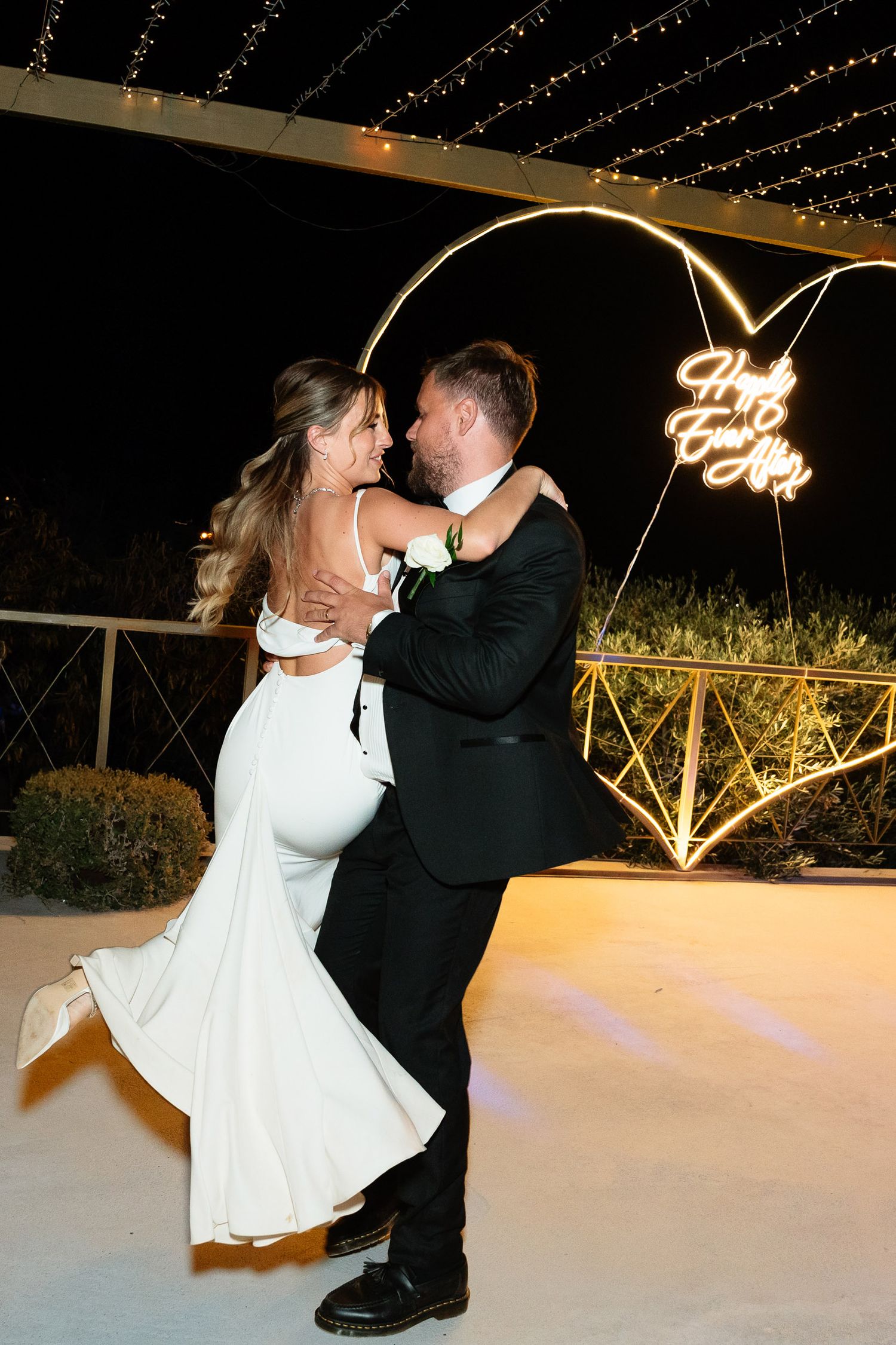 A bride and groom share a romantic dance sequence under twinkling lights at their wedding reception.