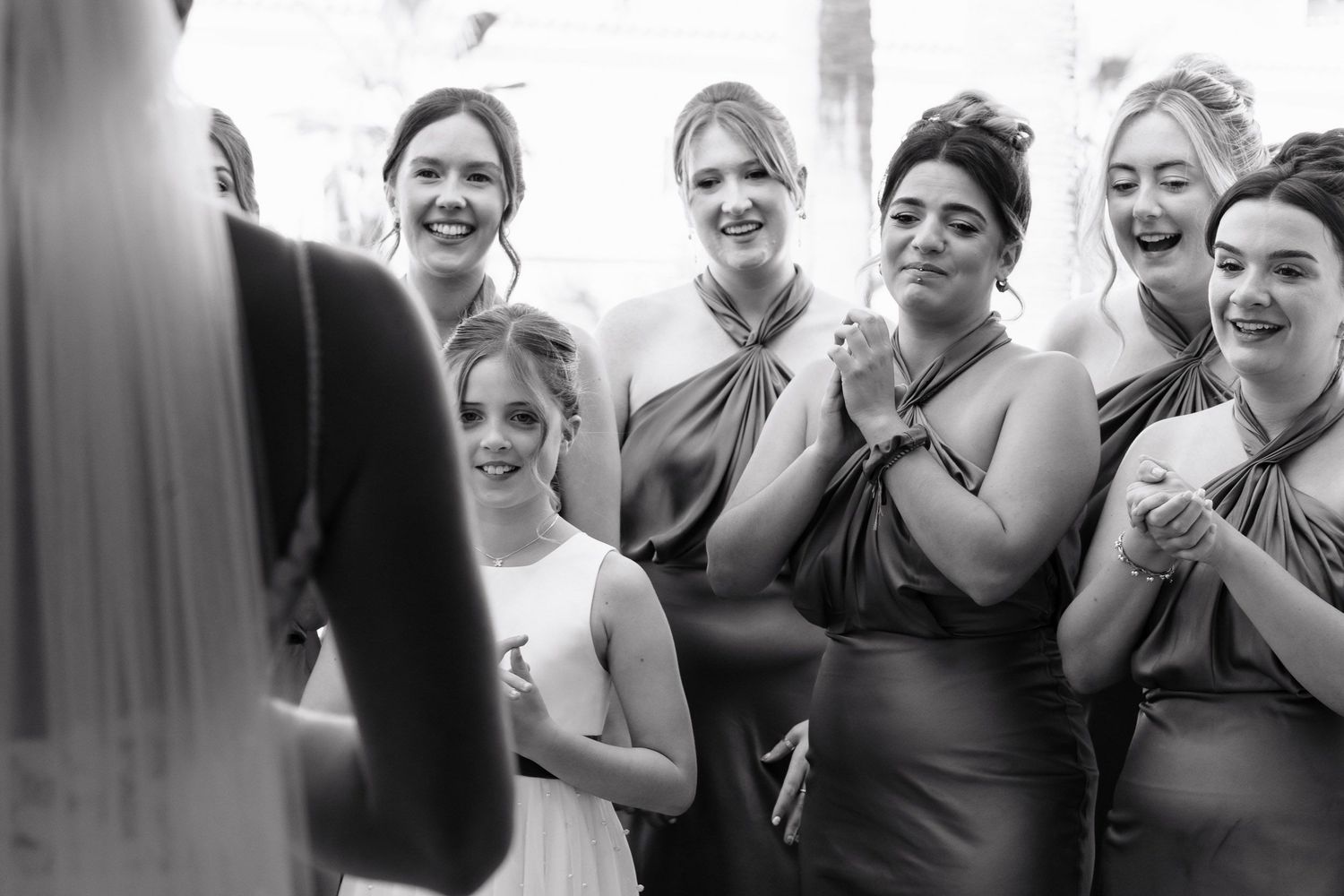 Black and white candid photo of bridesmaids and flower girl reacting emotionally during wedding ceremony.