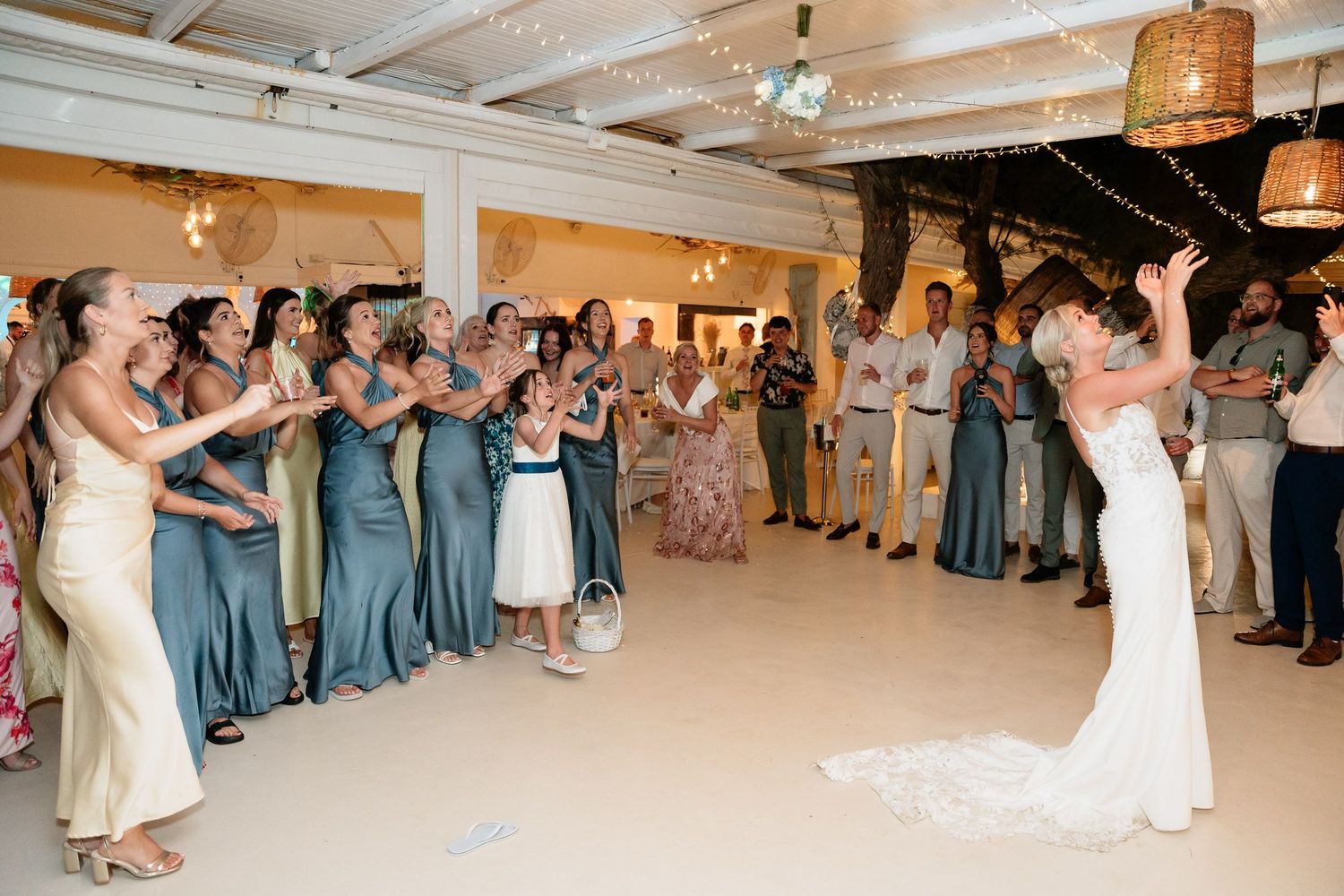 Wedding guests dancing in a line during a reception celebration with woven pendant lights hanging from wooden beams.