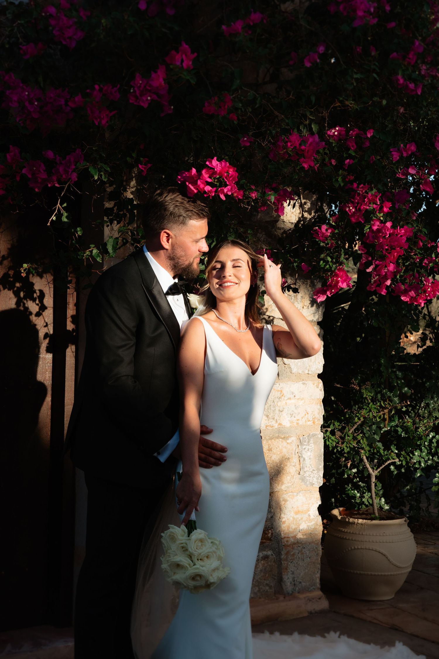 A romantic couple shares an intimate moment under vibrant pink bougainvillea flowers at dusk.