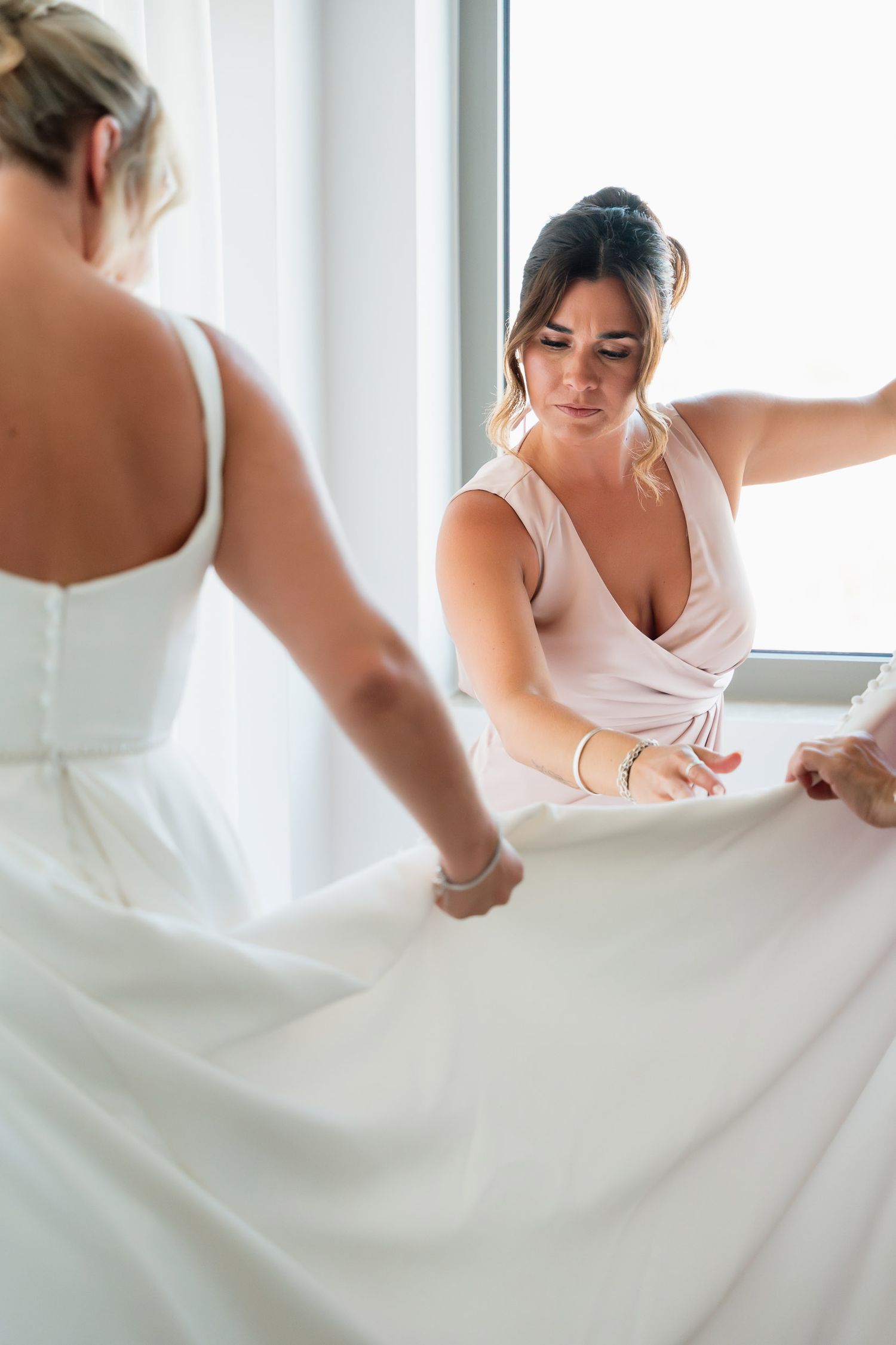 Close-up view of someone in a white wedding dress writing something while sitting at a table near windows.